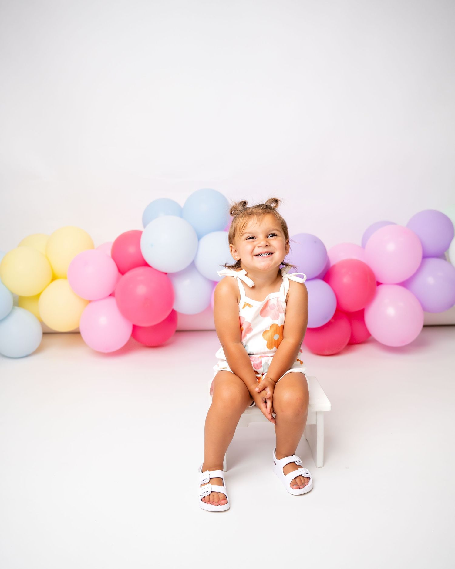 Metro Detroit children photographer Colorful pastel balloon garland decorates a white backdrop for a festive photo session.