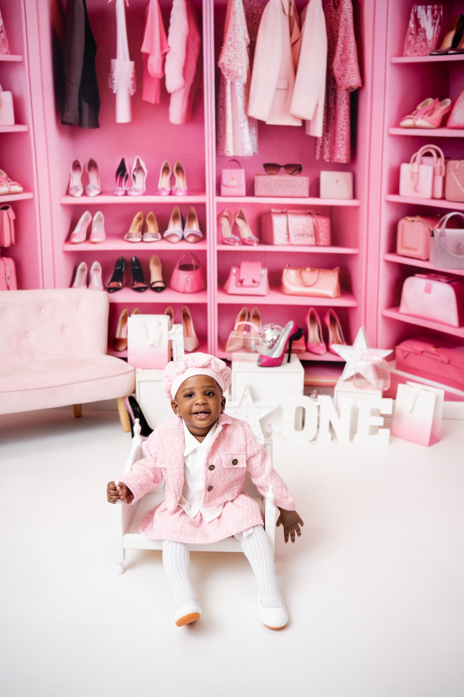Metro Detroit children photographer photographing a playful toddler in studio Pink walk-in closet filled with designer shoes,
