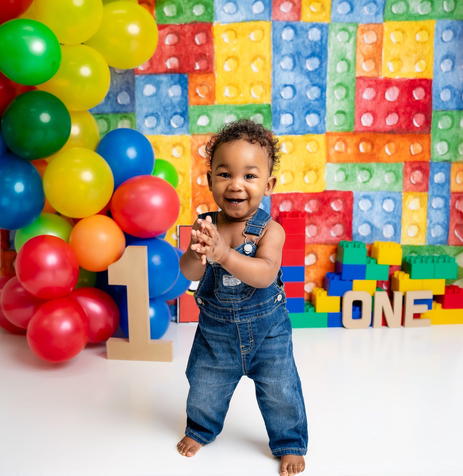 Metro Detroit children photographer photographing a playful toddler in Colorful first birthday setup with LEGO-inspired blocks and balloons.