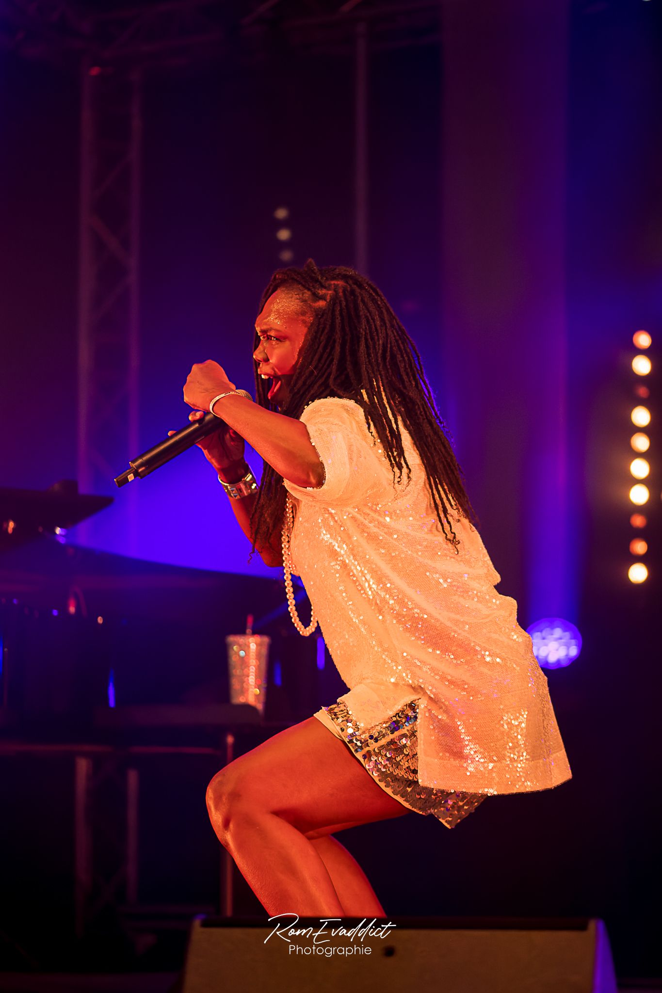 Femme créole chanteuse en robe courte à paillette blanche accroupie le poing en l'air durant concert de jazz- photo spectacle événementiel