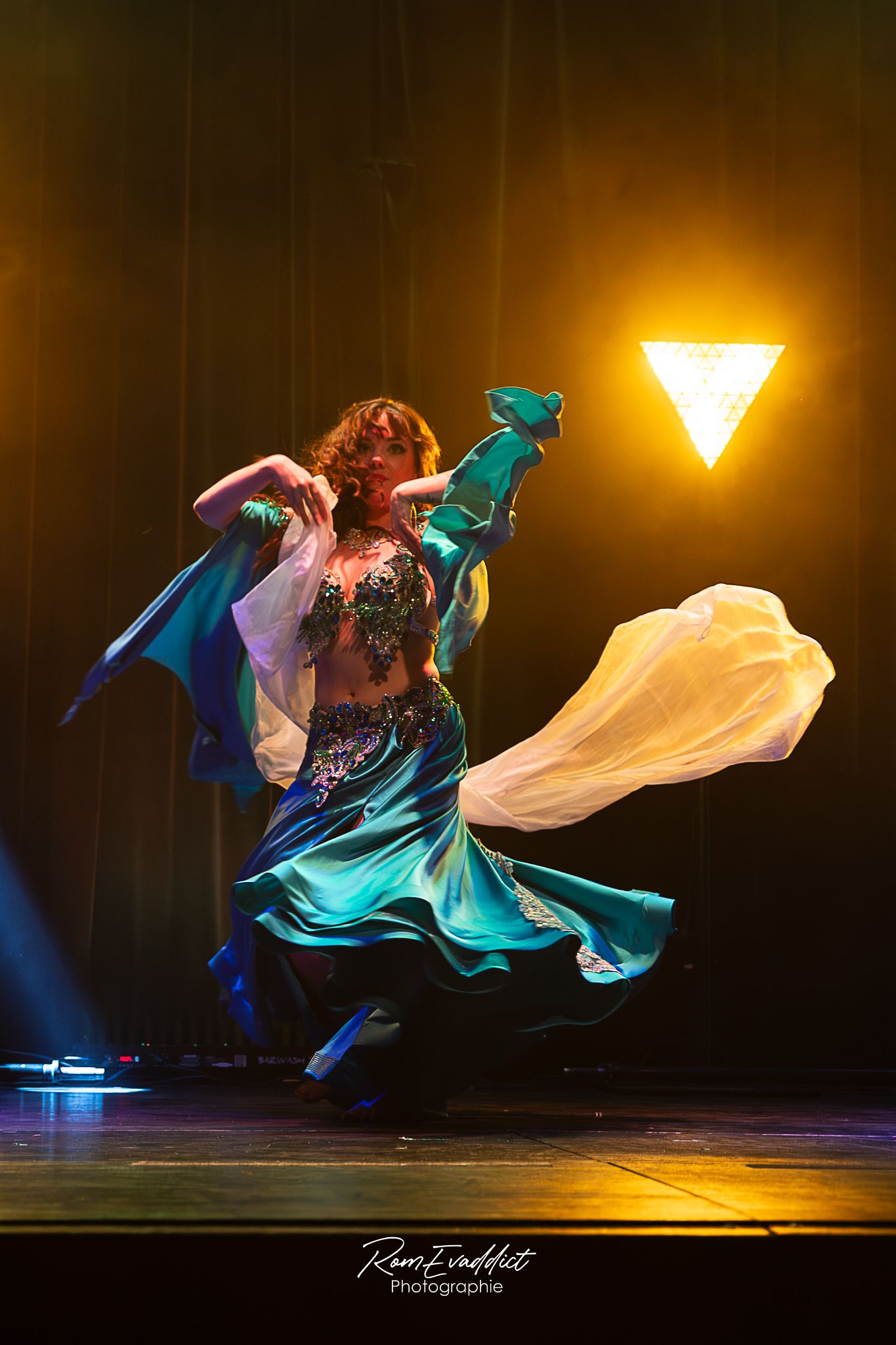 photo sur scène danseuse du ventre grande robe satinée bleu et verte - lumière colorée - photo artiste événementiel concerts spectacles
