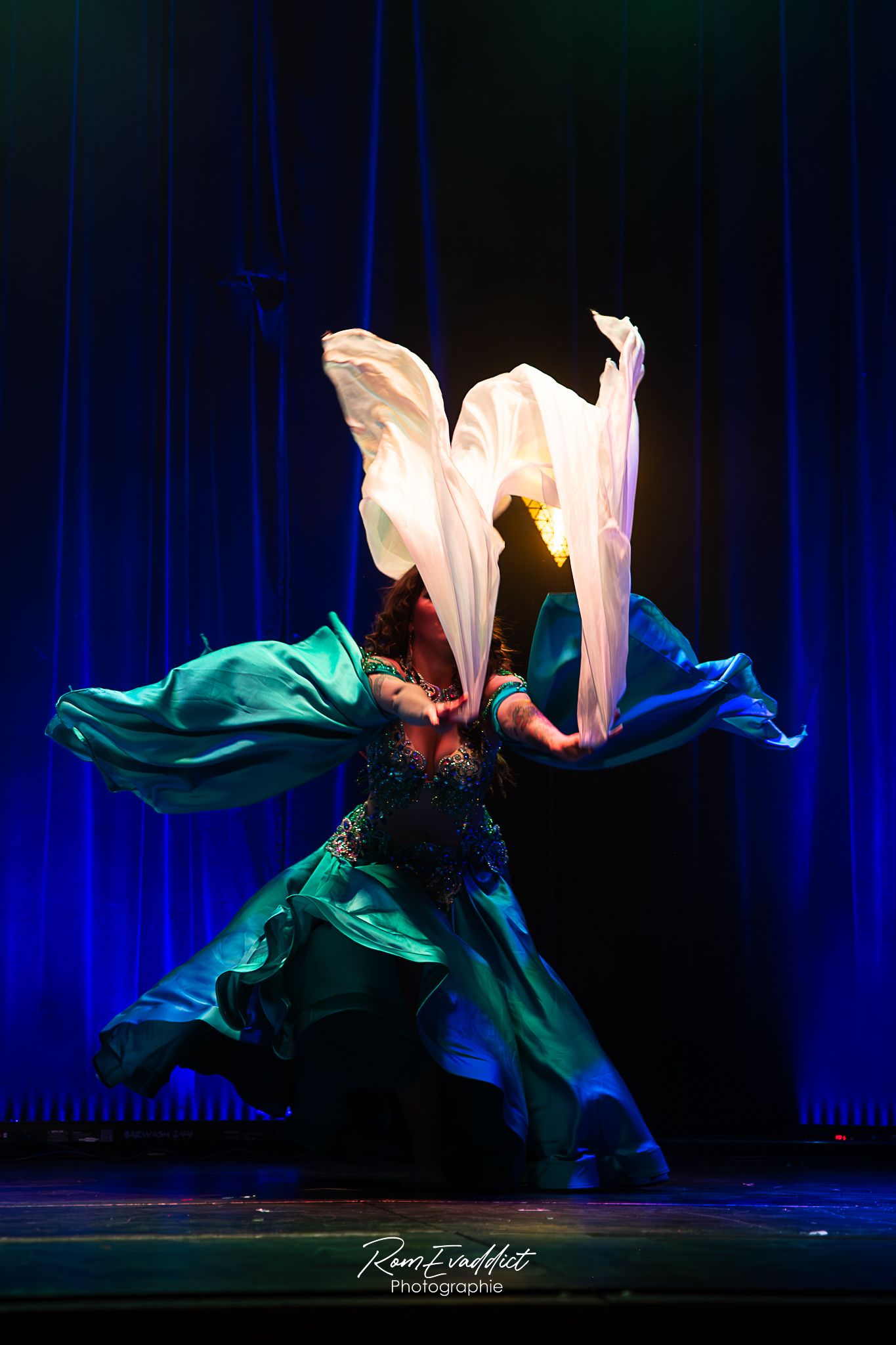 photo sur scène danseuse du ventre grande robe satinée bleu et verte - lumière colorée - photo artiste événementiel concerts spectacles