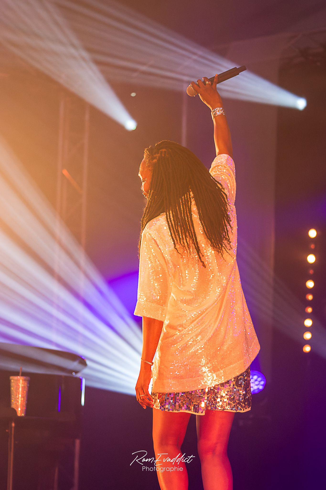 Femme créole chanteuse en robe courte à paillette blanche accroupie le poing en l'air durant concert de jazz- photo spectacle événementiel