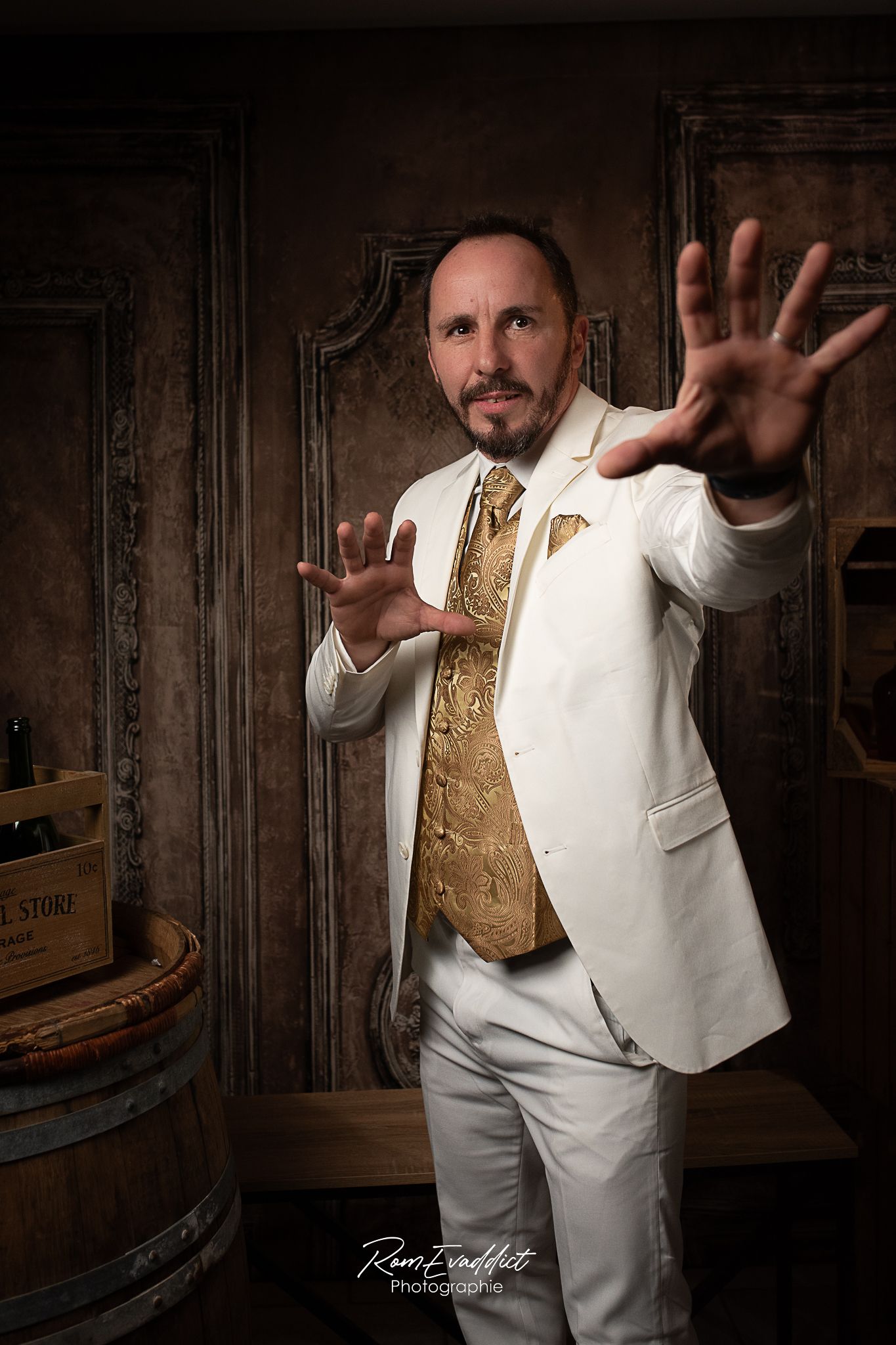 homme en costume trois pièces blanc avec gilet doré se tenant debout devant un fond effet boiserie pour une photo portrait corporate