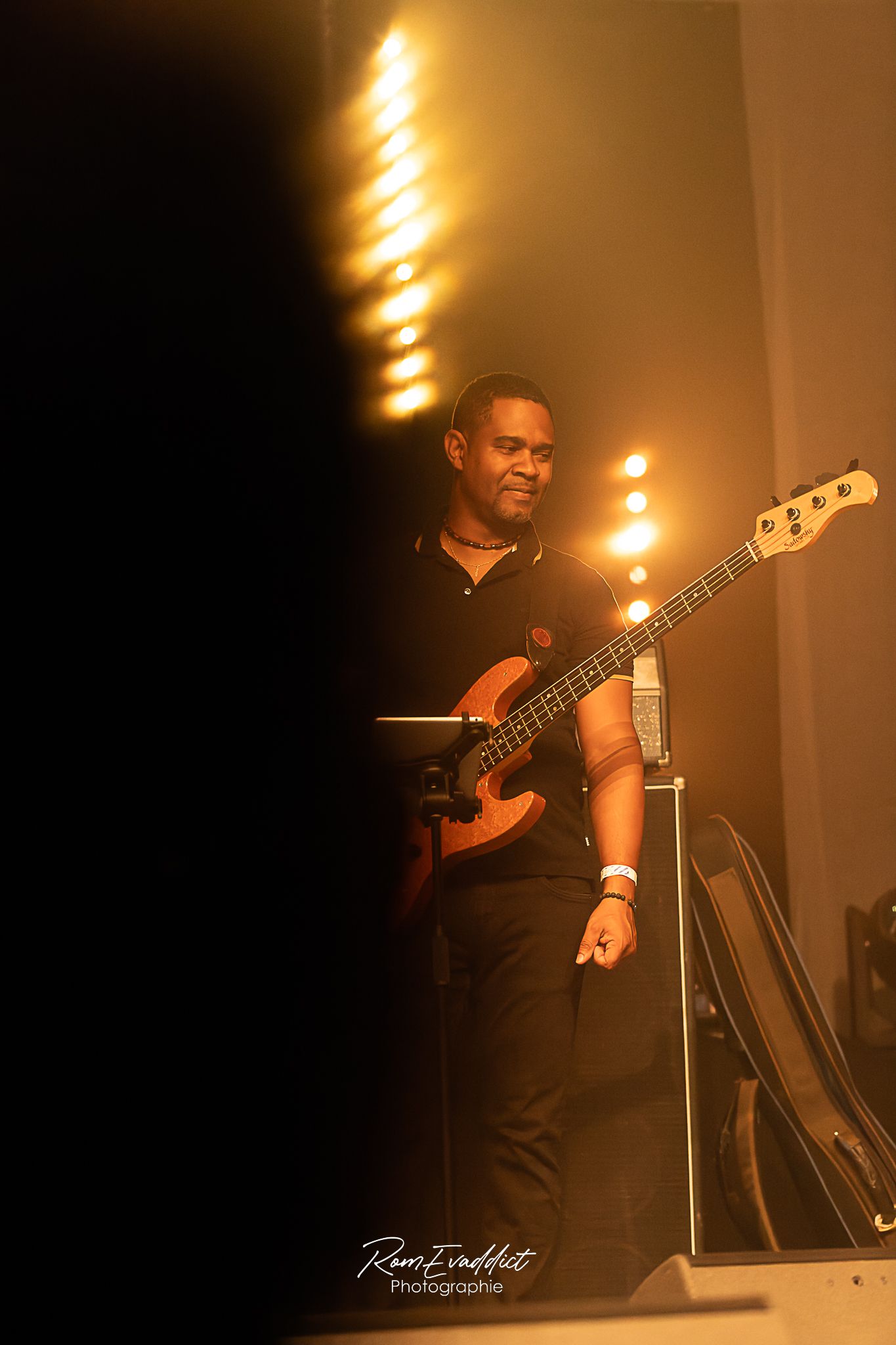 Homme créole musicien guitariste pantalon et polo noir durant concert de jazz-éclairage scénique chaud- photo spectacle événementiel
