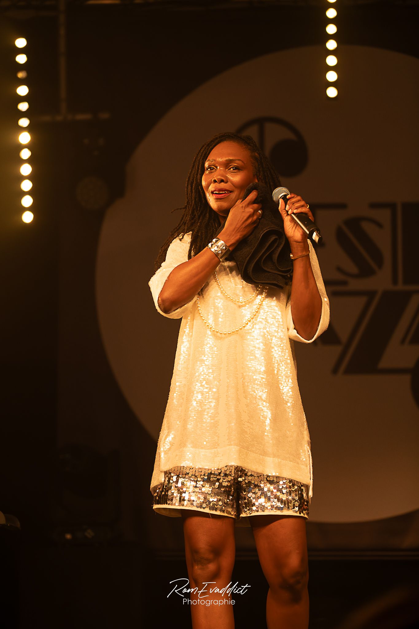 Femme créole cheveux long chanteuse en robe courte à paillette blanche debout sur scène durant concert de jazz- photo spectacle événementiel