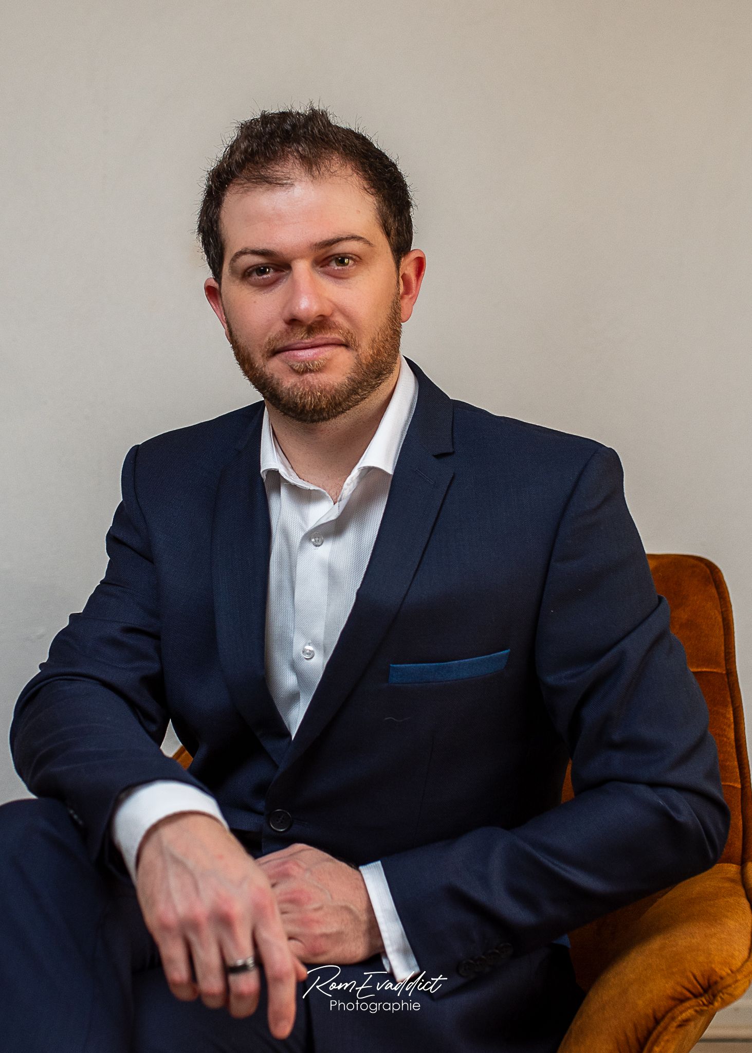 homme en costume bleu et chemise blanche assis dans un fauteuil pour une photo portrait corporate d'entreprise business