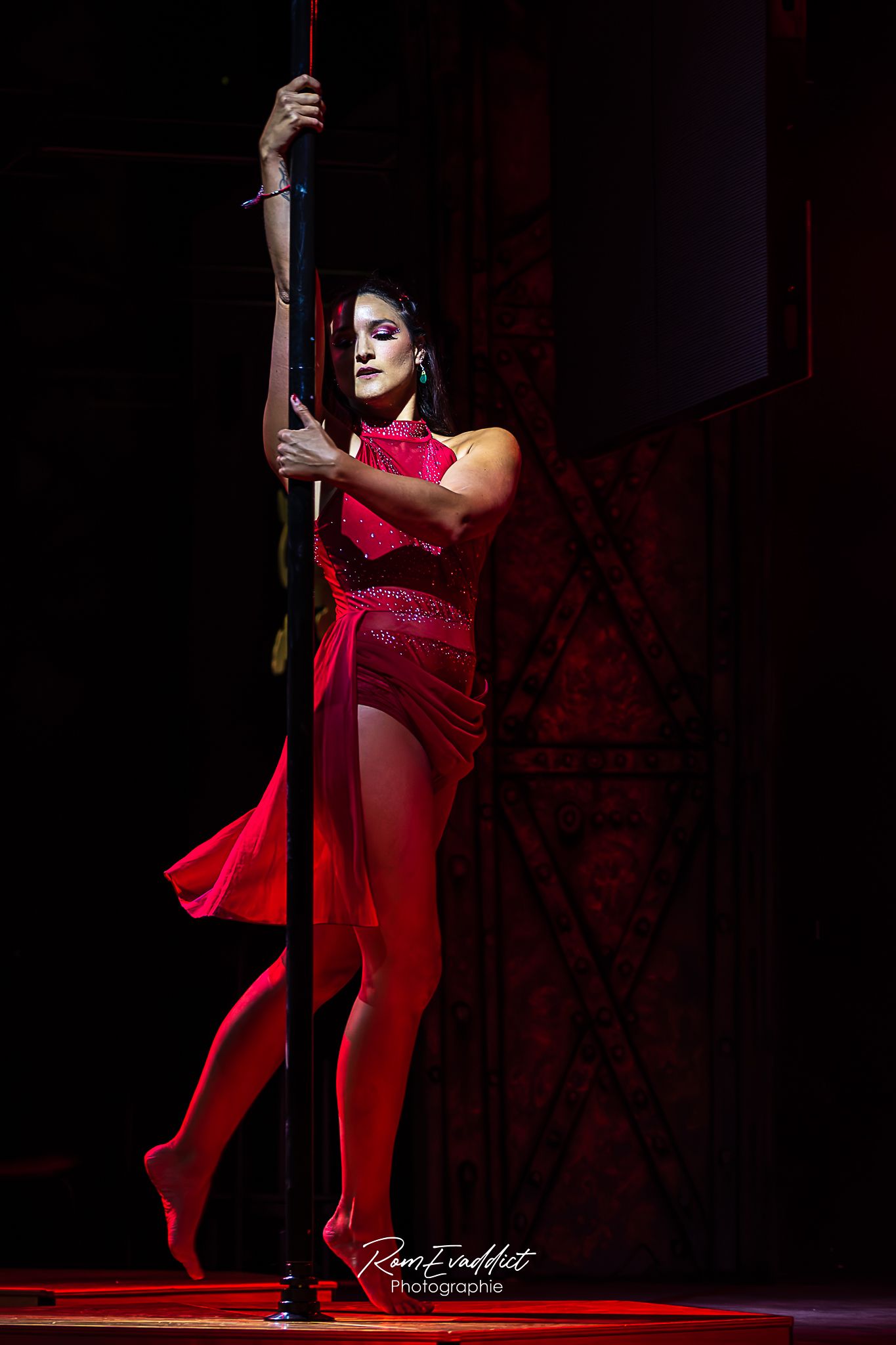 photo femme robe rouge se tenant debout appuyée à une barre de pole dance sur scène. Spectacle événementiel - artistes