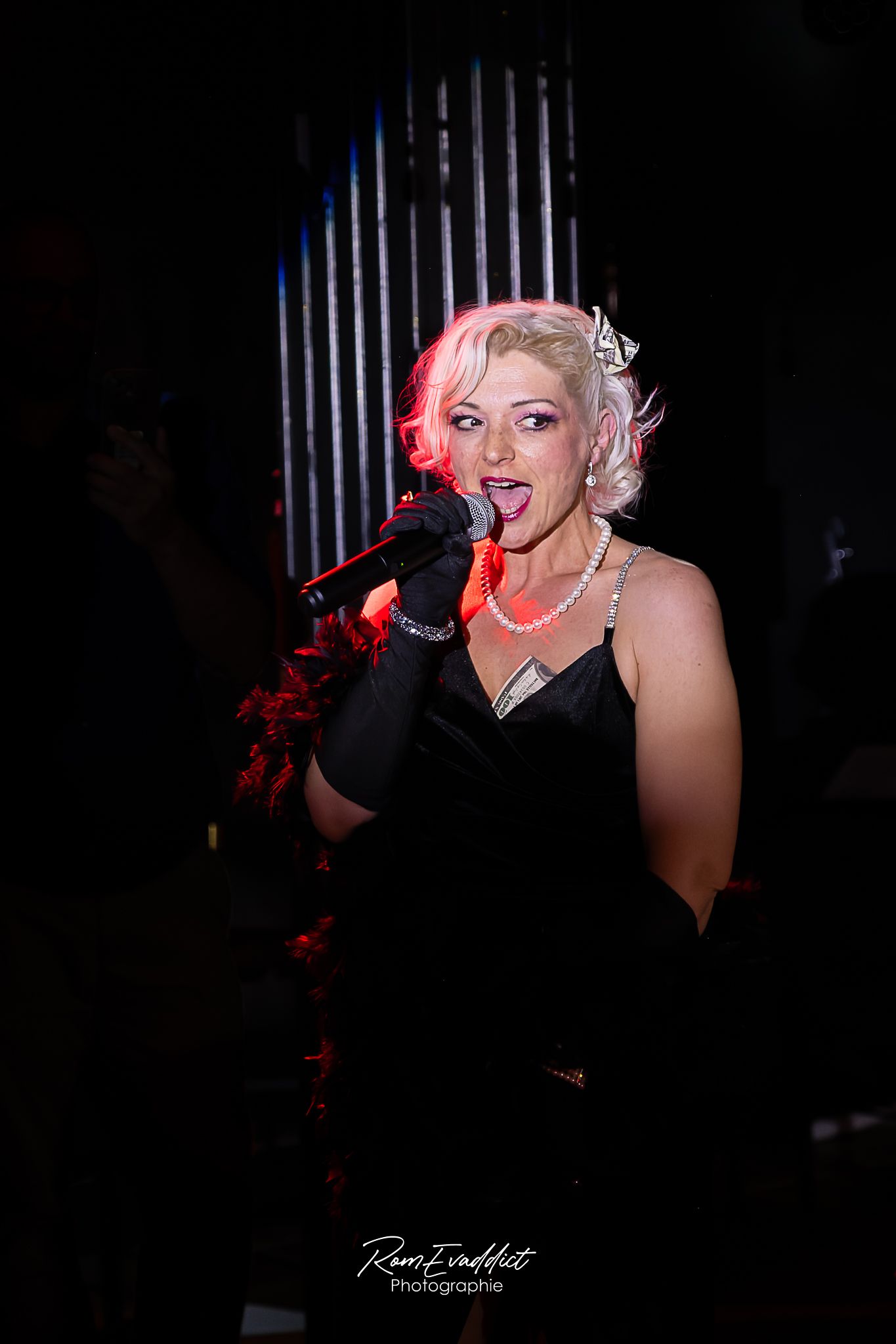 photo chanteuse de cabaret-blonde robe longue à strass noirs- chantant durant spectacle de cabaret- lumière poursuite-événementiel-artistes