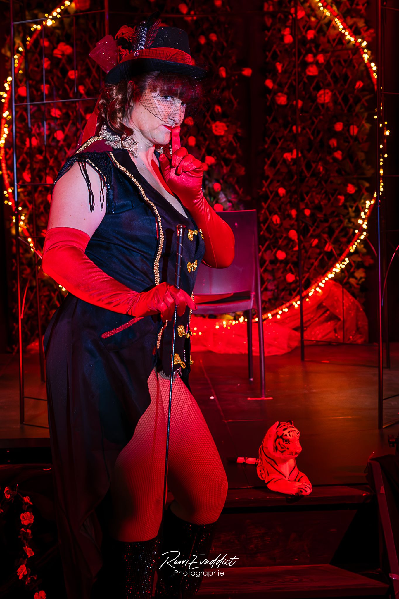 Femme danseuse effeuilleuse burlesque veste longue et haut de forme noir gant rouge, dresseuse de tigre devant cage-spectacles événementiel