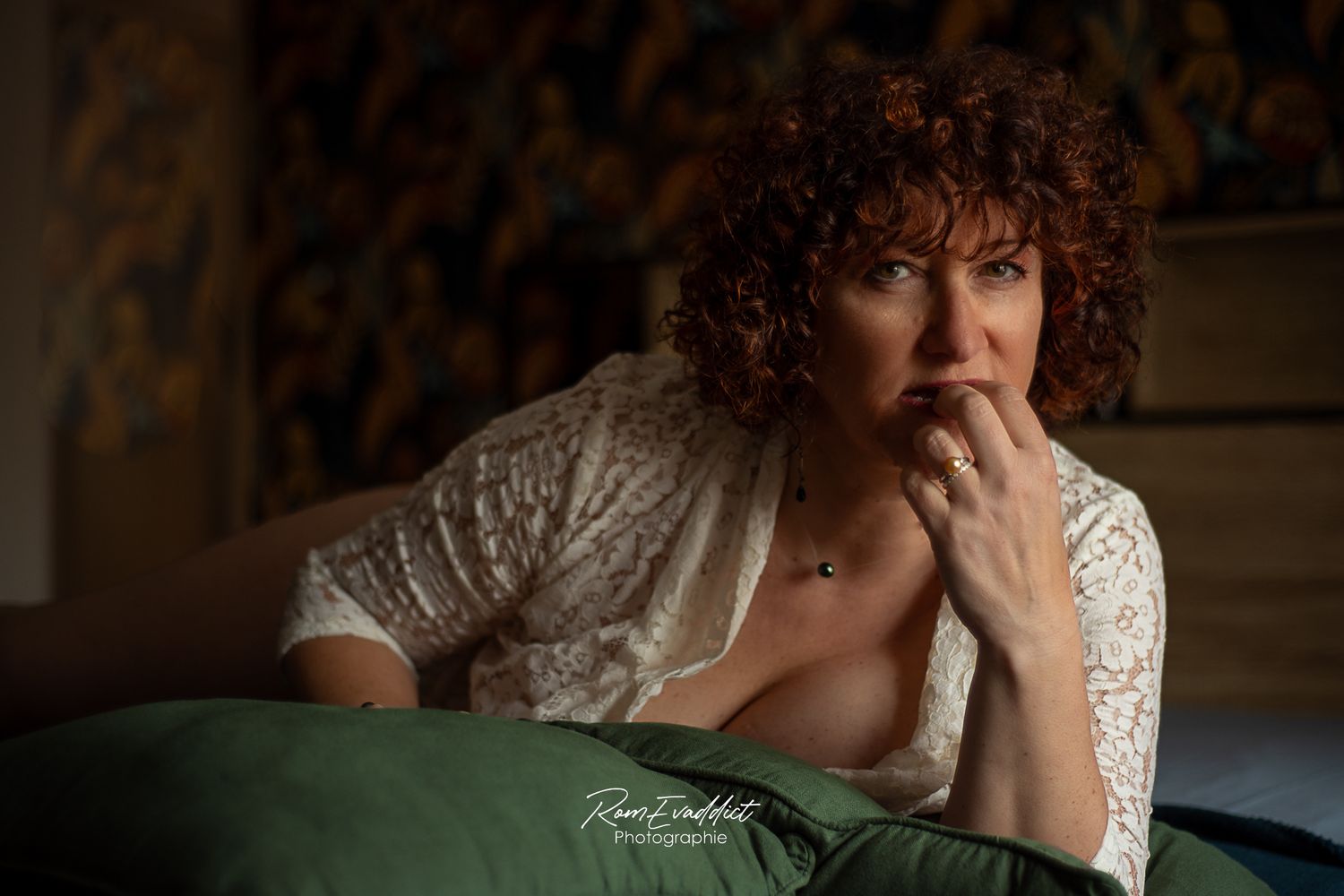 femme cheveux roux bouclés chemise blanche ouverte, accoudée sur un lit, décolleté caché par une coussin vert-portrait boudoir intimiste