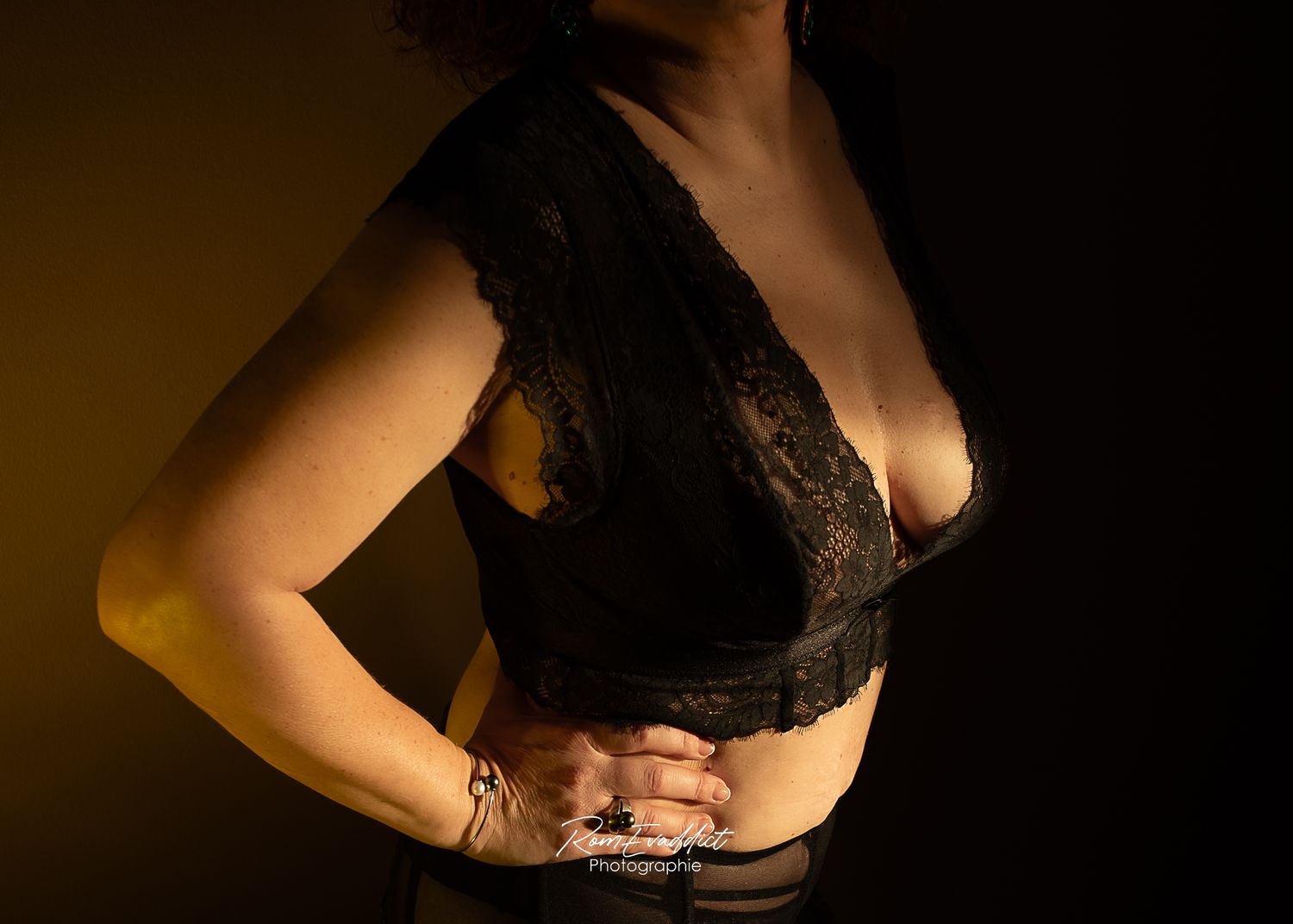 femme en ensemble dentelle noire debout dans l'ombre éclairée par un rayon lumineux, la main posée sur la hanche-portrait boudoir intimiste
