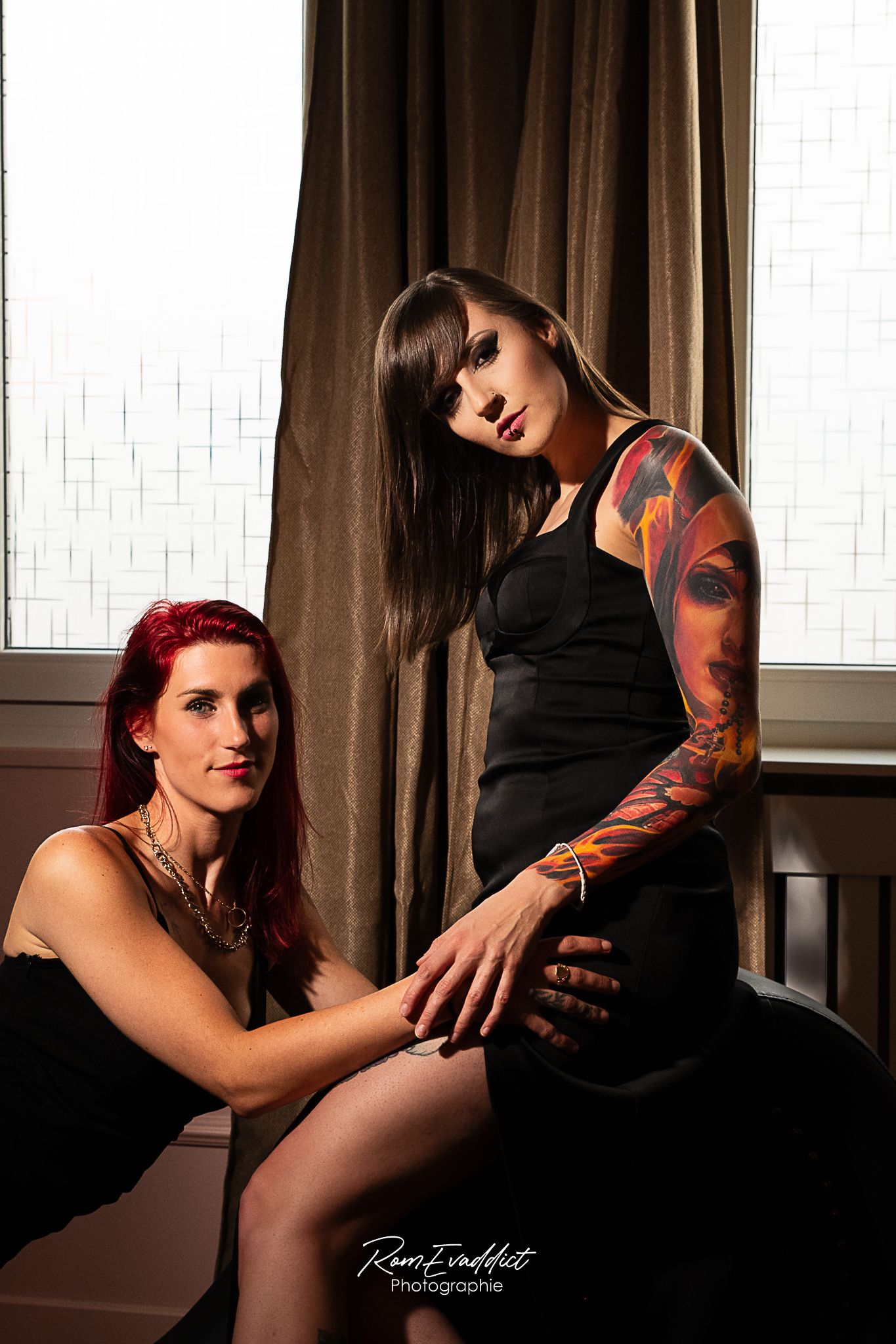 deux femmes se faisant face sur un fauteuil tentra-robes longues noires- épaule tatouée-éclairage tamisé- portrait boudoir intmiste