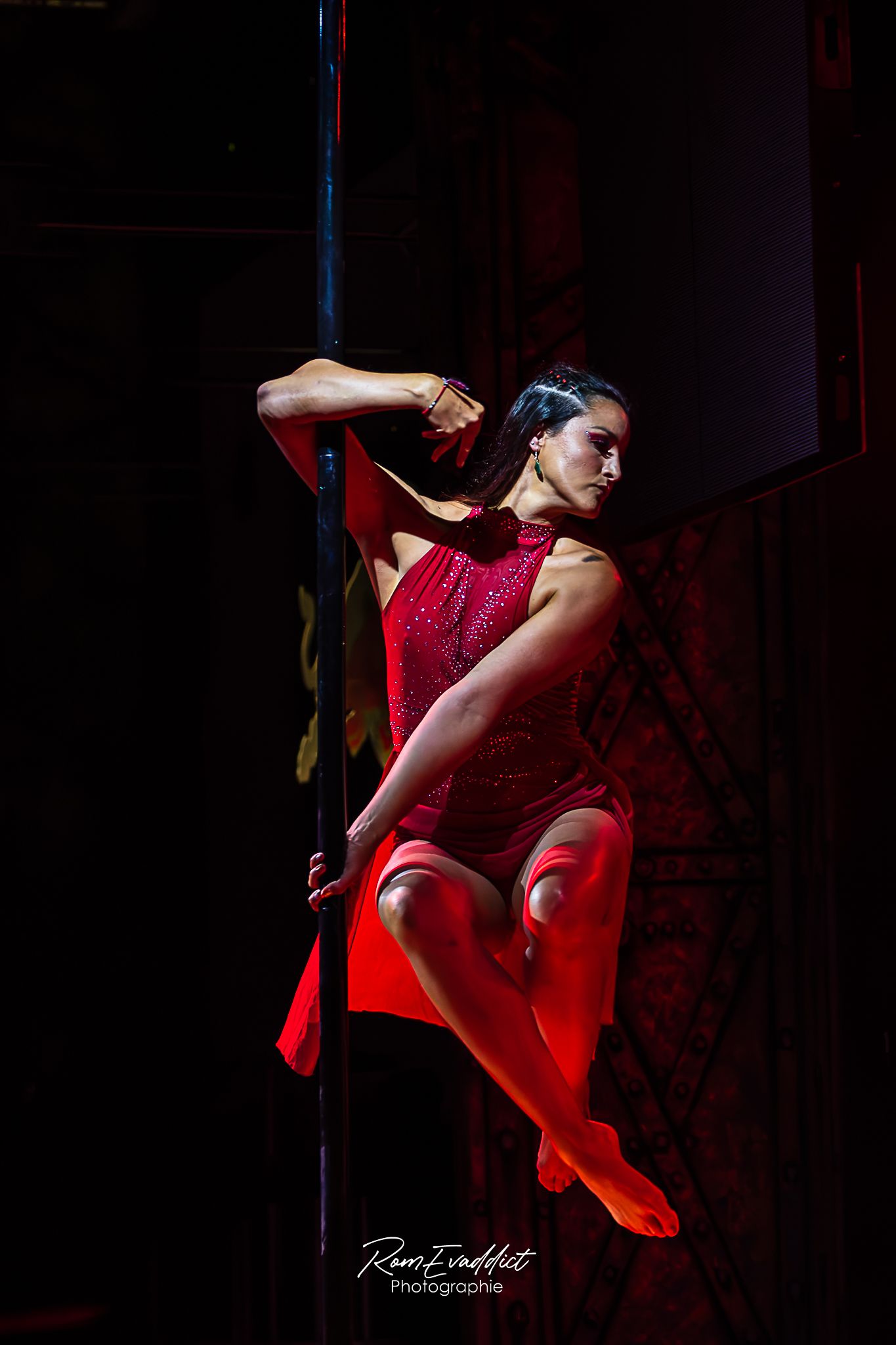 femme en robe rouge effectuant une figure de pole dance en position assise se tenant à la barre de pole dance-Spectacle événementiel