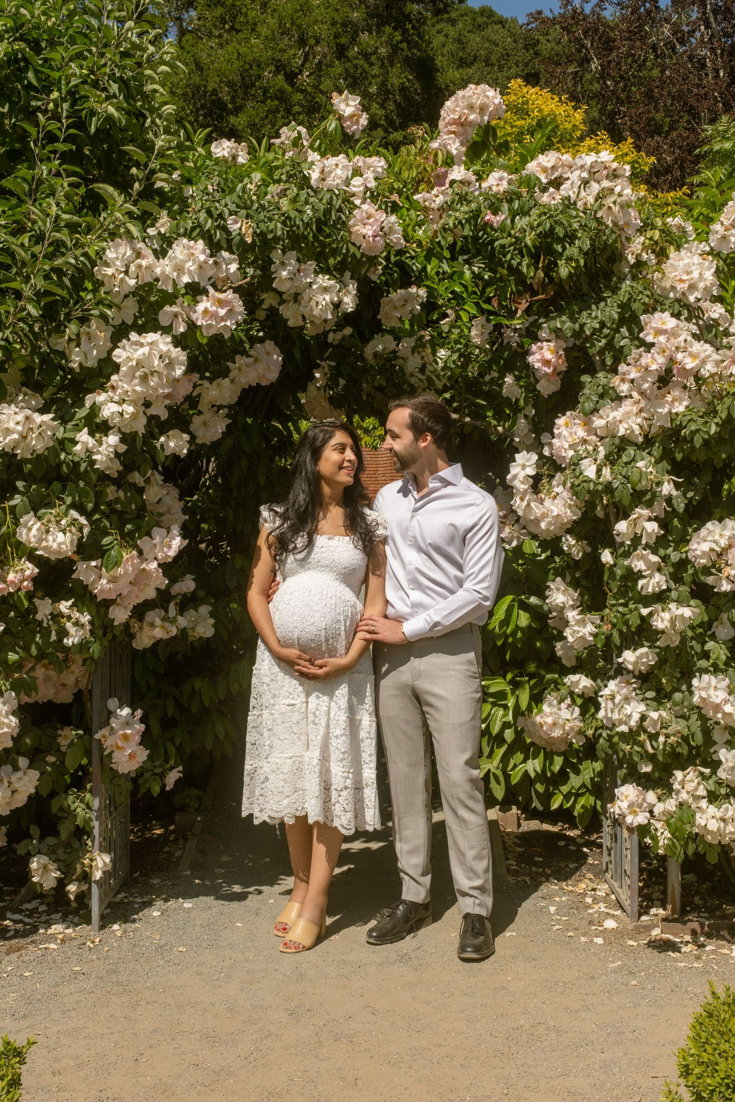 Couple posing together against wall of blooming pink roses in garden.