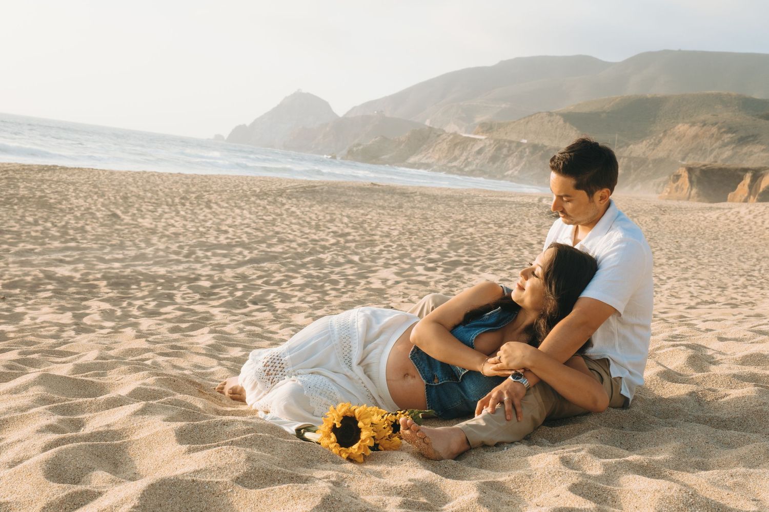 A couple relaxes on the beach sand during a sunset photoshoot.