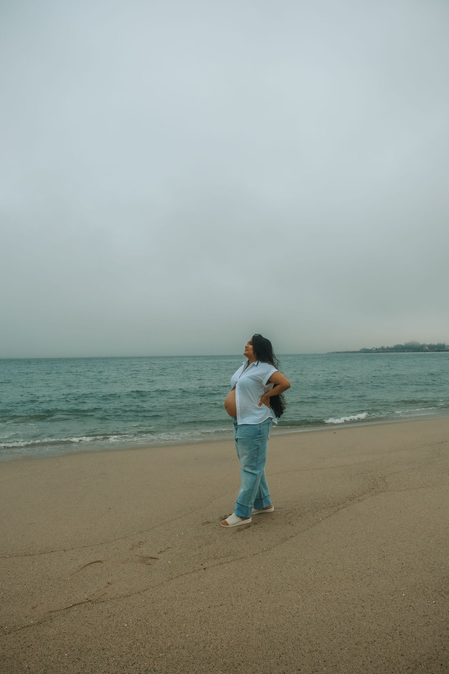 A person in light blue clothing dances joyfully on a misty beach by the ocean.