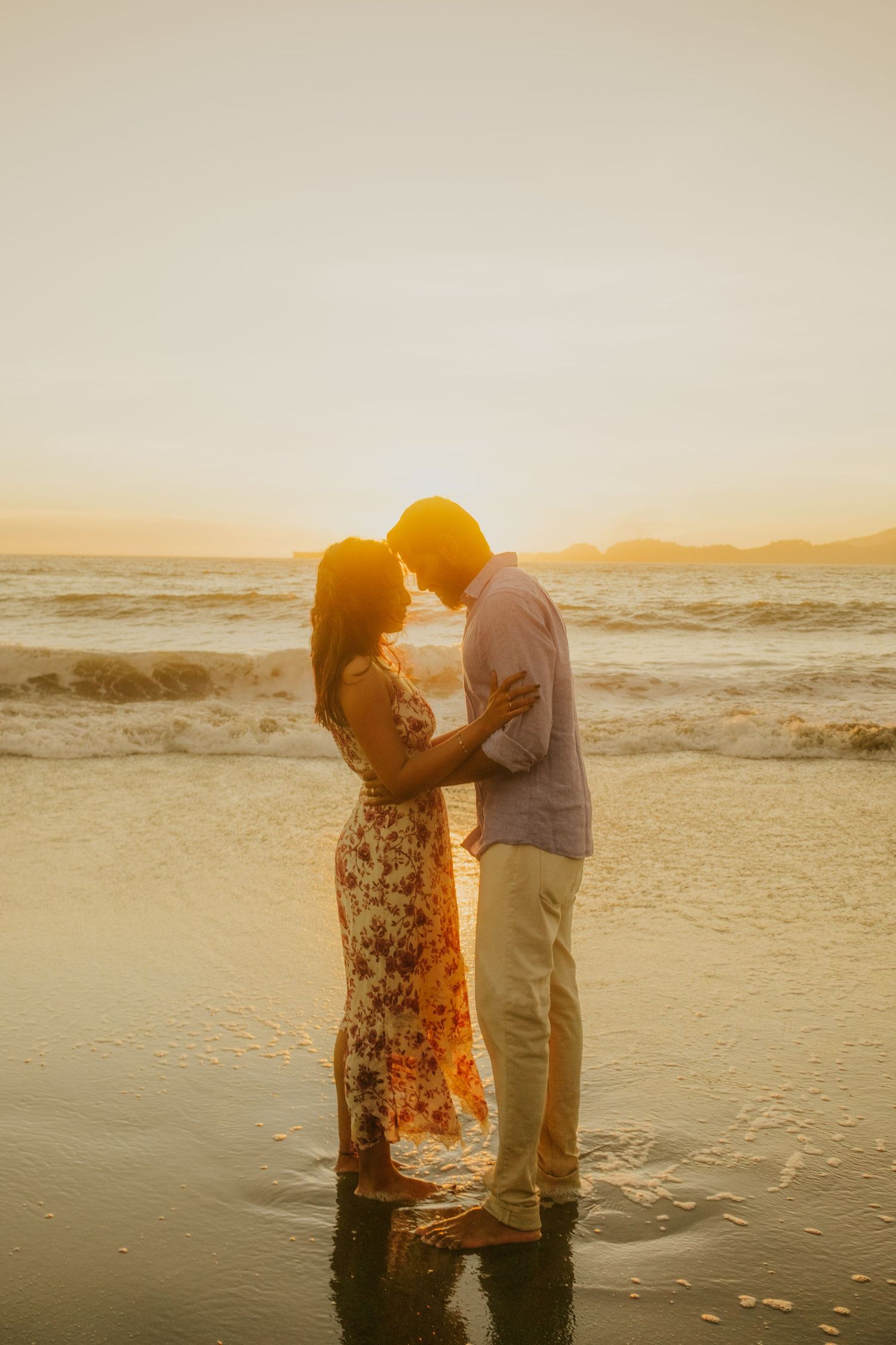 Couple standing in shallow ocean water during golden hour sunset.