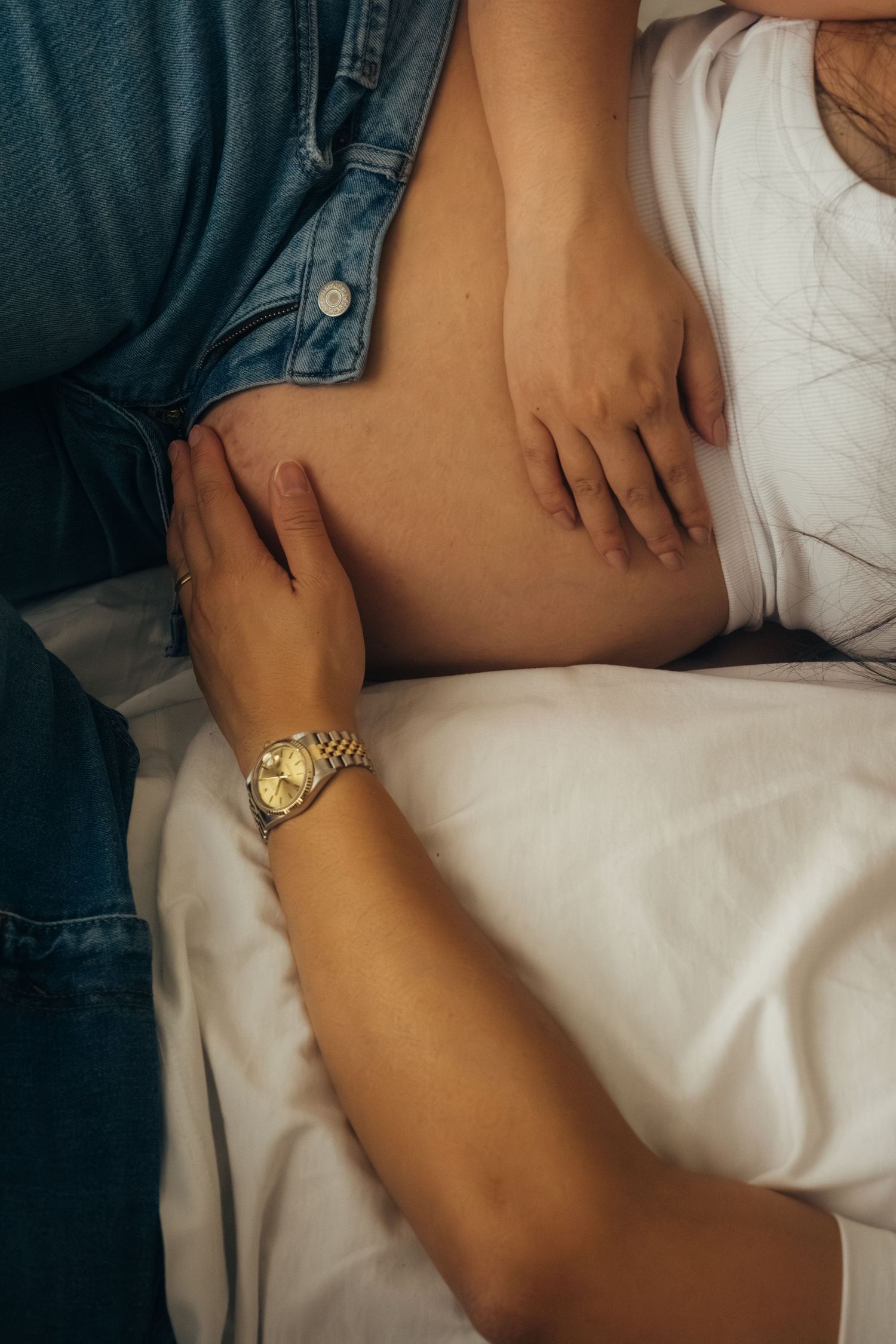 Close-up of hands gently resting on pregnant belly with gold watch detail.