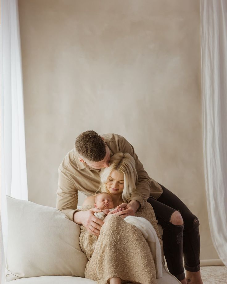 A parent and baby lie together on a cozy white bed while sharing tender moments in soft natural light.