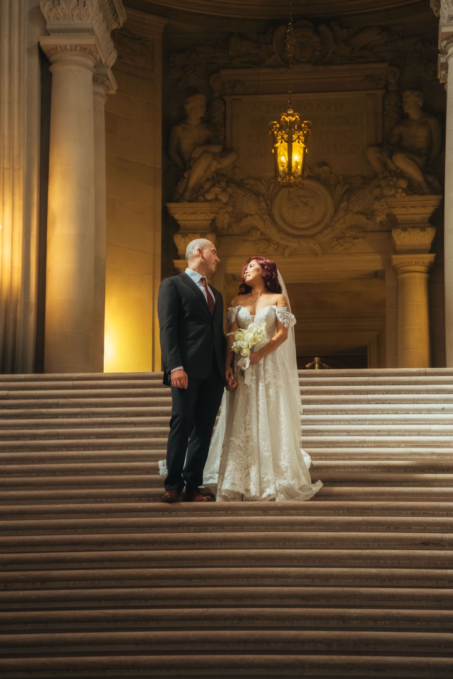 Newlyweds share romantic moments on wide marble steps in a grand historic building.