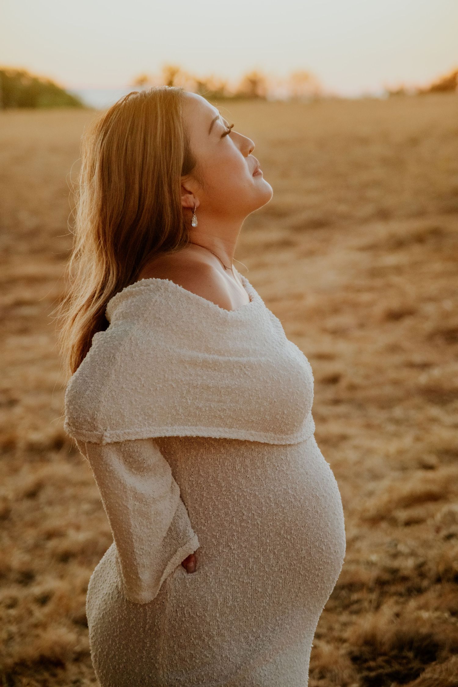 A person in a cozy cream sweater poses against a warm sunset backdrop.