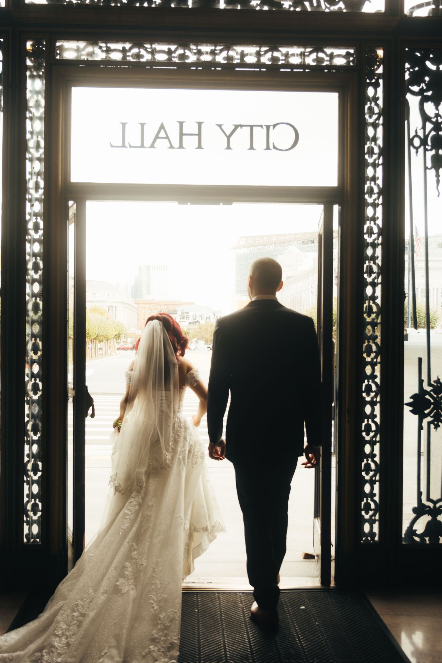 Wedding couple walks through elegant doorway with trailing bridal gown and veil.