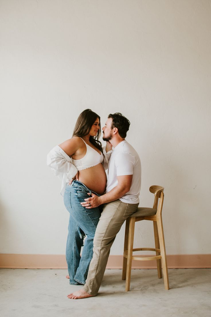 Candid maternity photos of couple sharing tender moments in minimal studio setting.