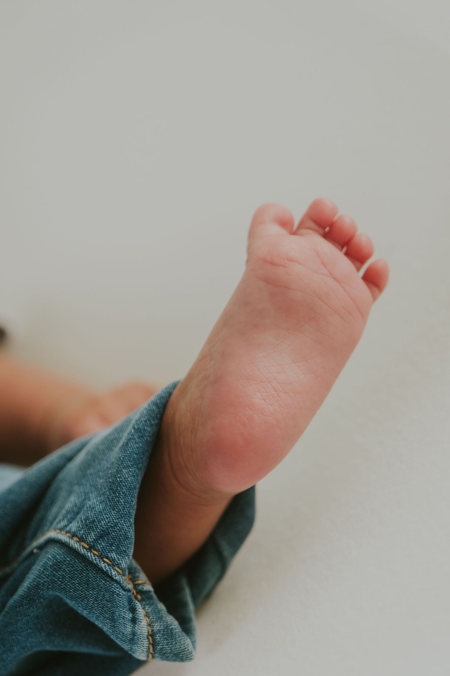Small baby feet peeking out from blue denim fabric in natural light.