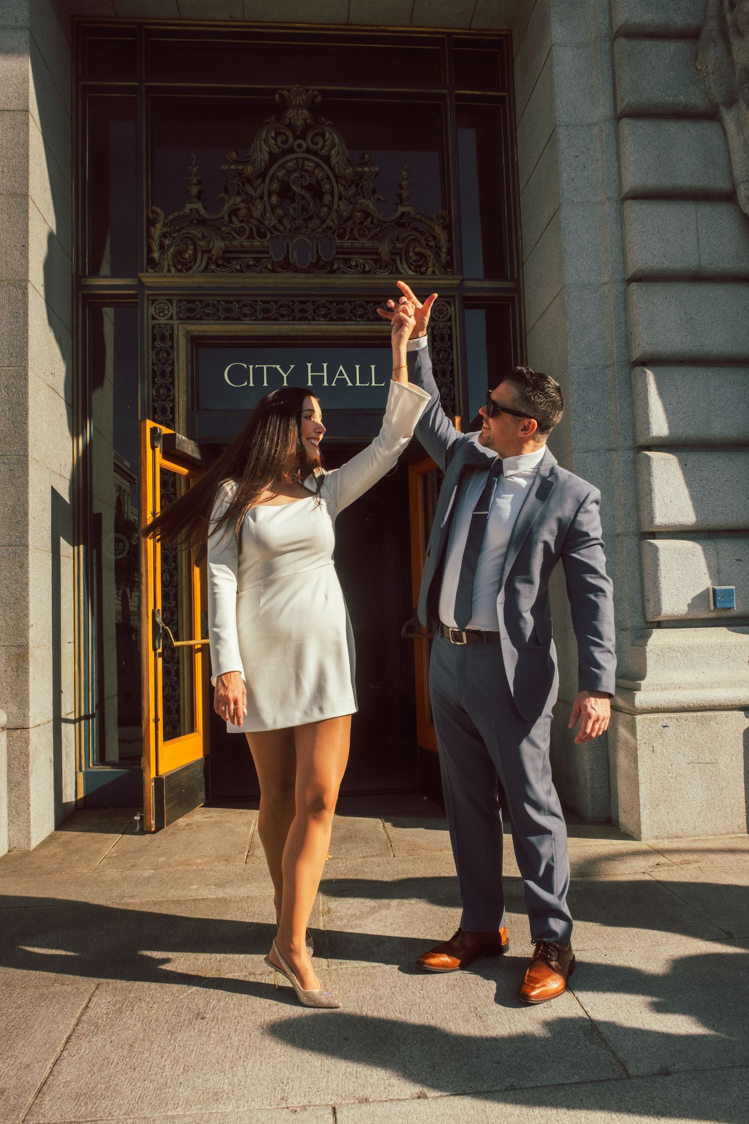 Joyful dance moves outside City Hall's entrance in bright sunlight.