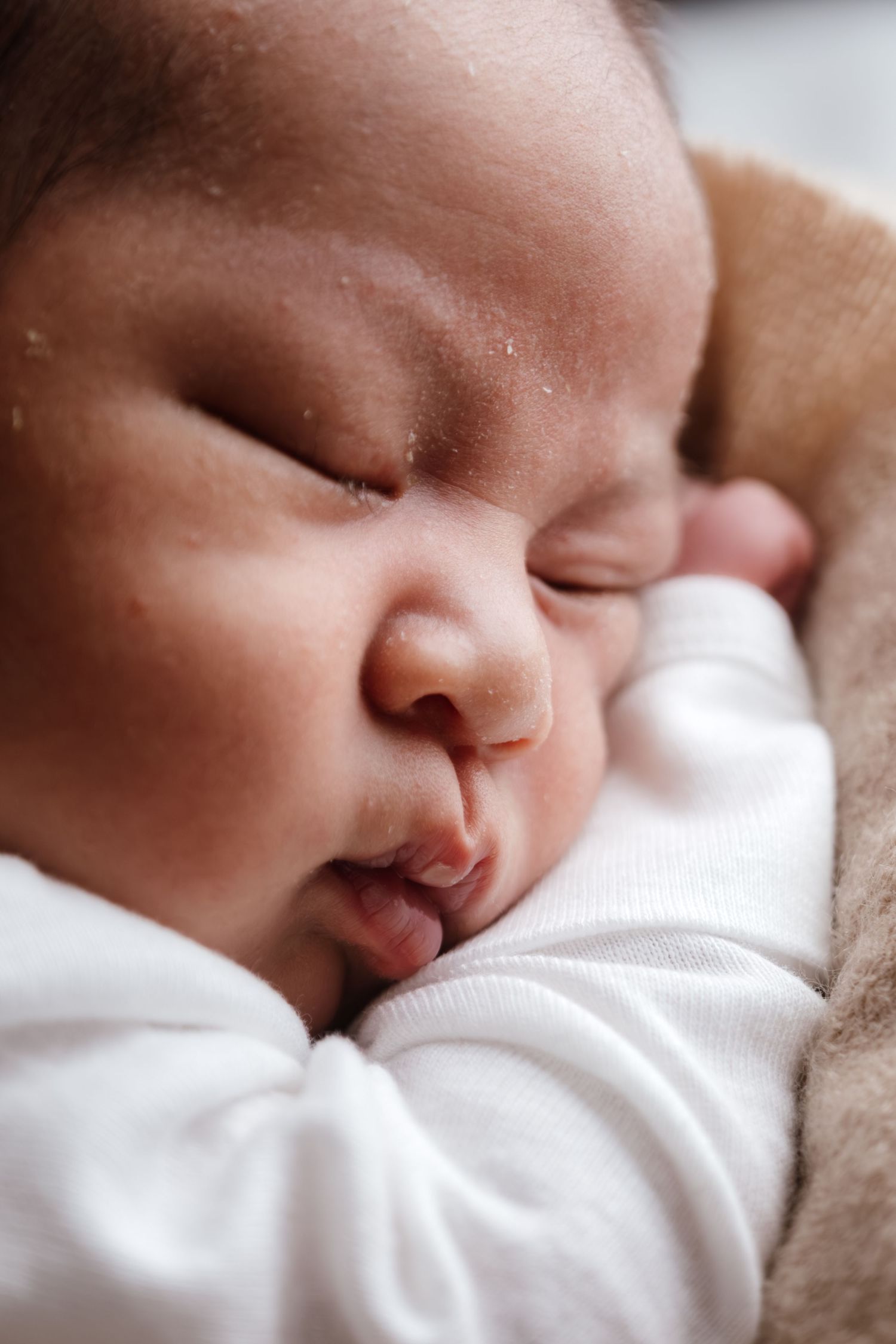 A peaceful newborn baby sleeping soundly, dressed in white, with delicate features and soft skin.
