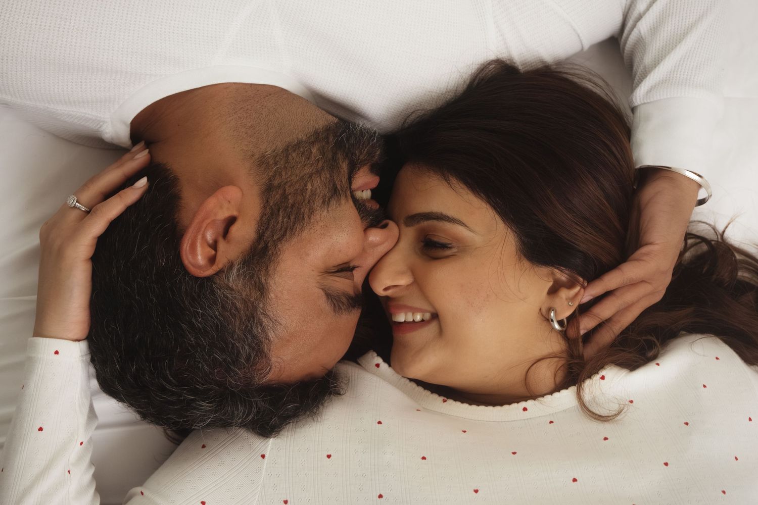 Couple lying close together on white surface in intimate moment.