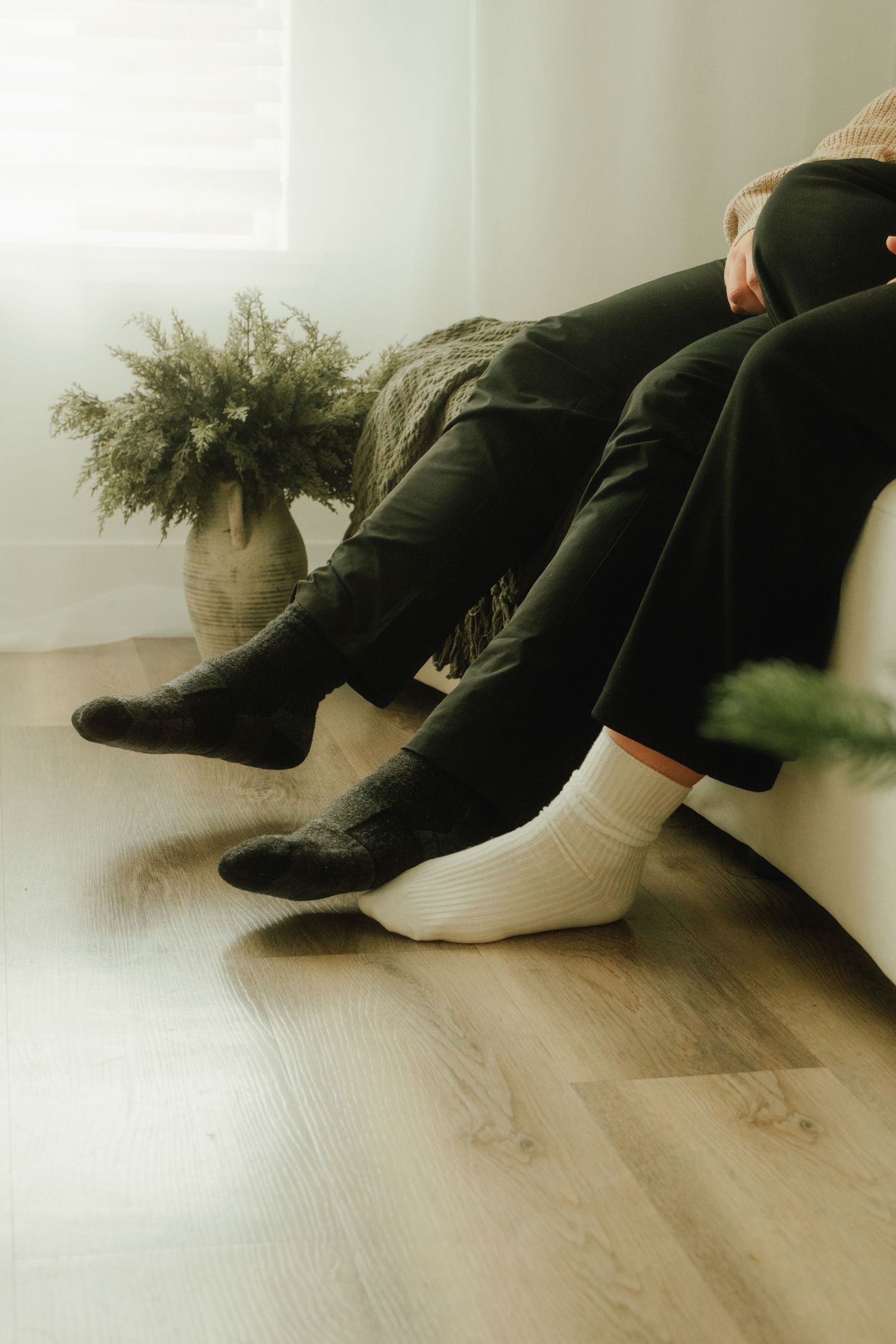 Close-up of feet in white socks on wooden floor next to potted plant.
