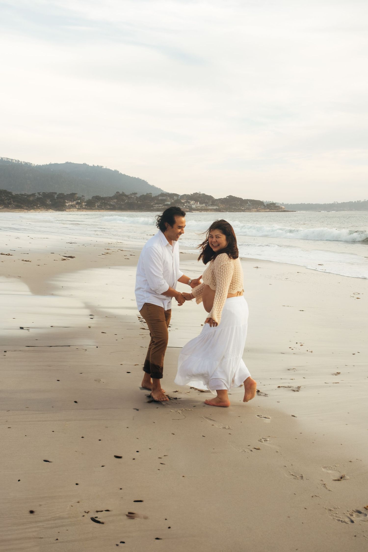 Family plays together on empty beach with mountains visible in background.