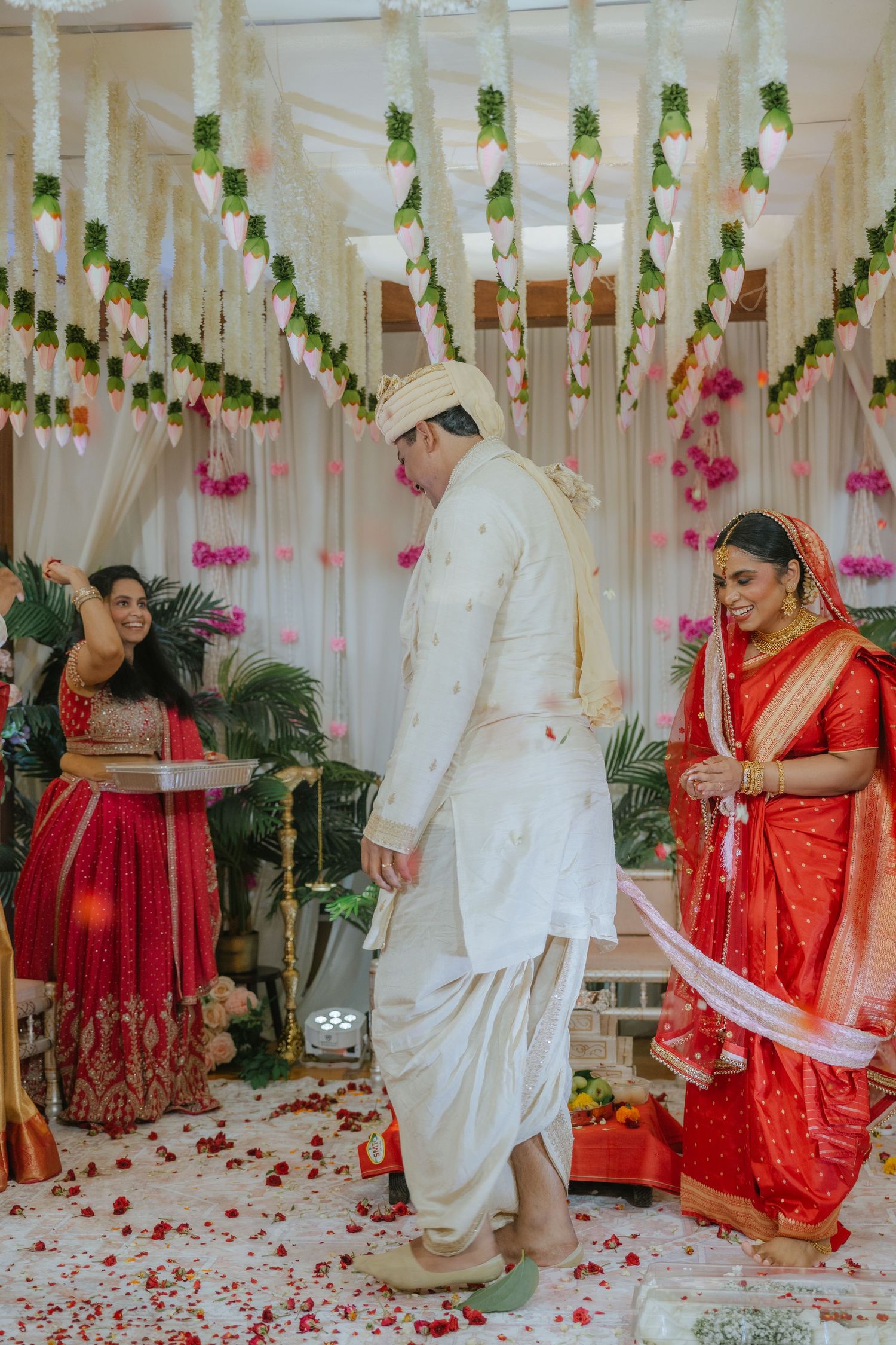 Bride in red saree and groom in white dhoti perform traditional Indian wedding ceremony under floral decorations.