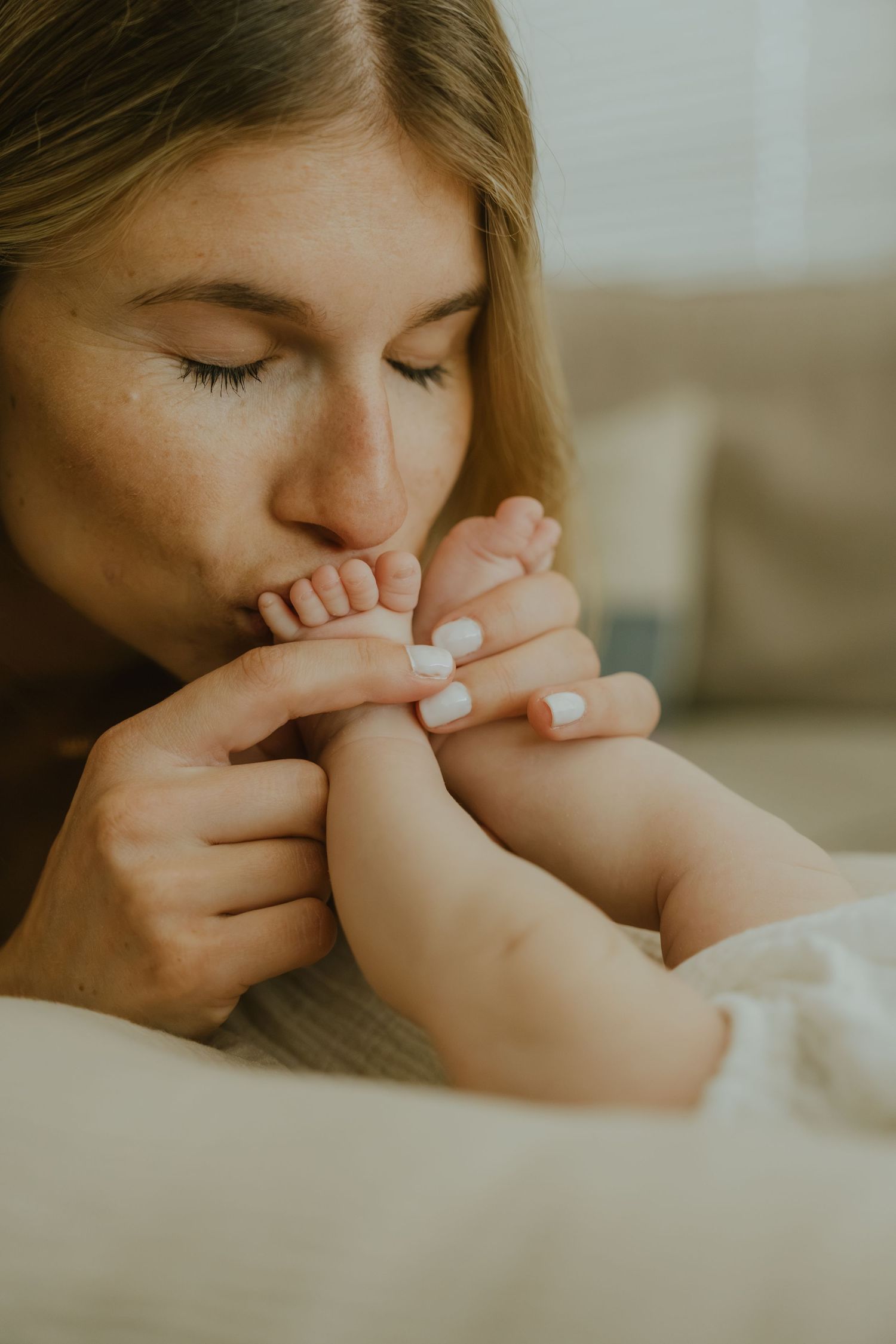 A tender mother gently kisses her newborn baby's tiny feet while holding them lovingly in her hands.