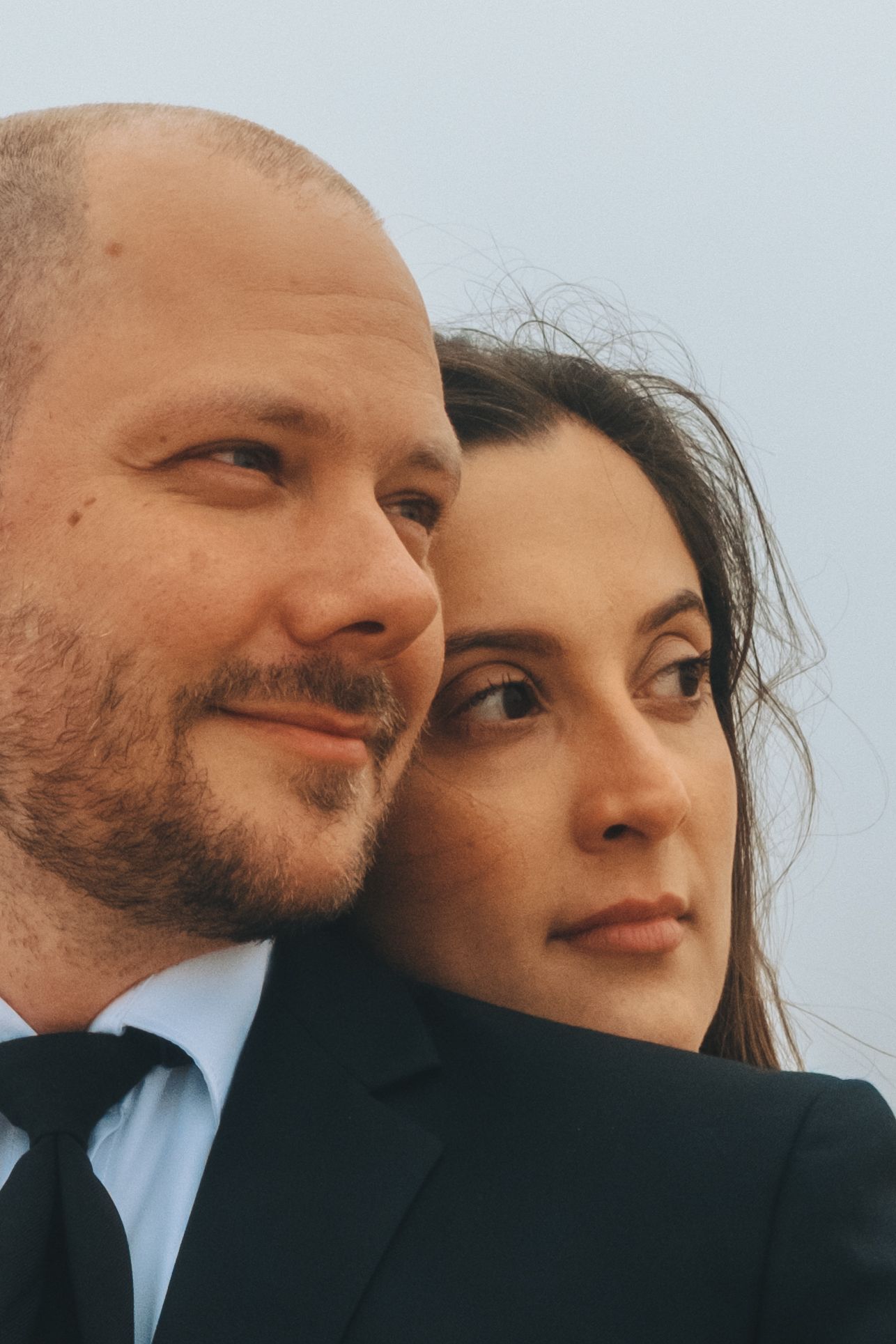 Close-up candid portrait of a couple against sky background.