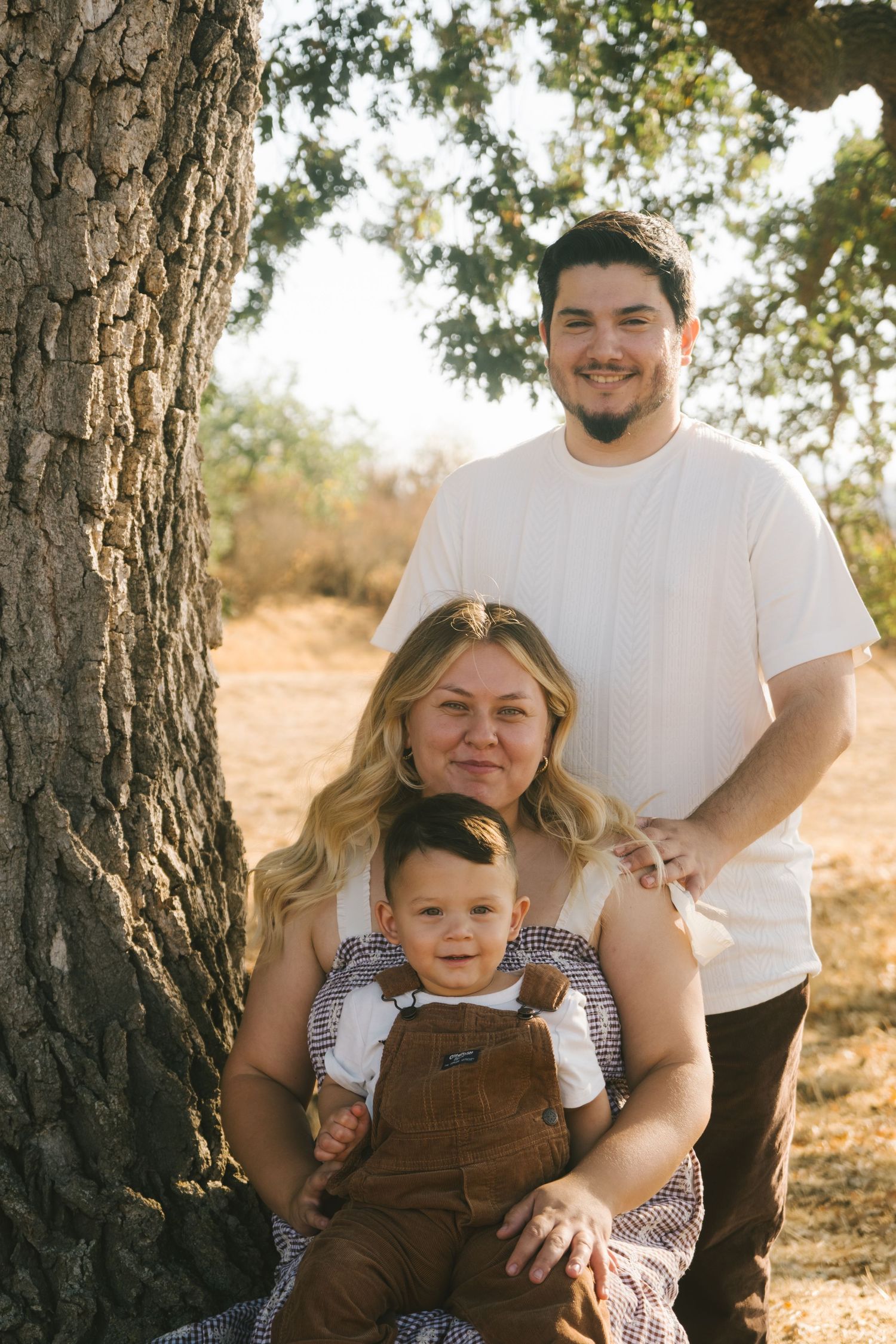 A family sits together against a tree trunk during an outdoor photo session.