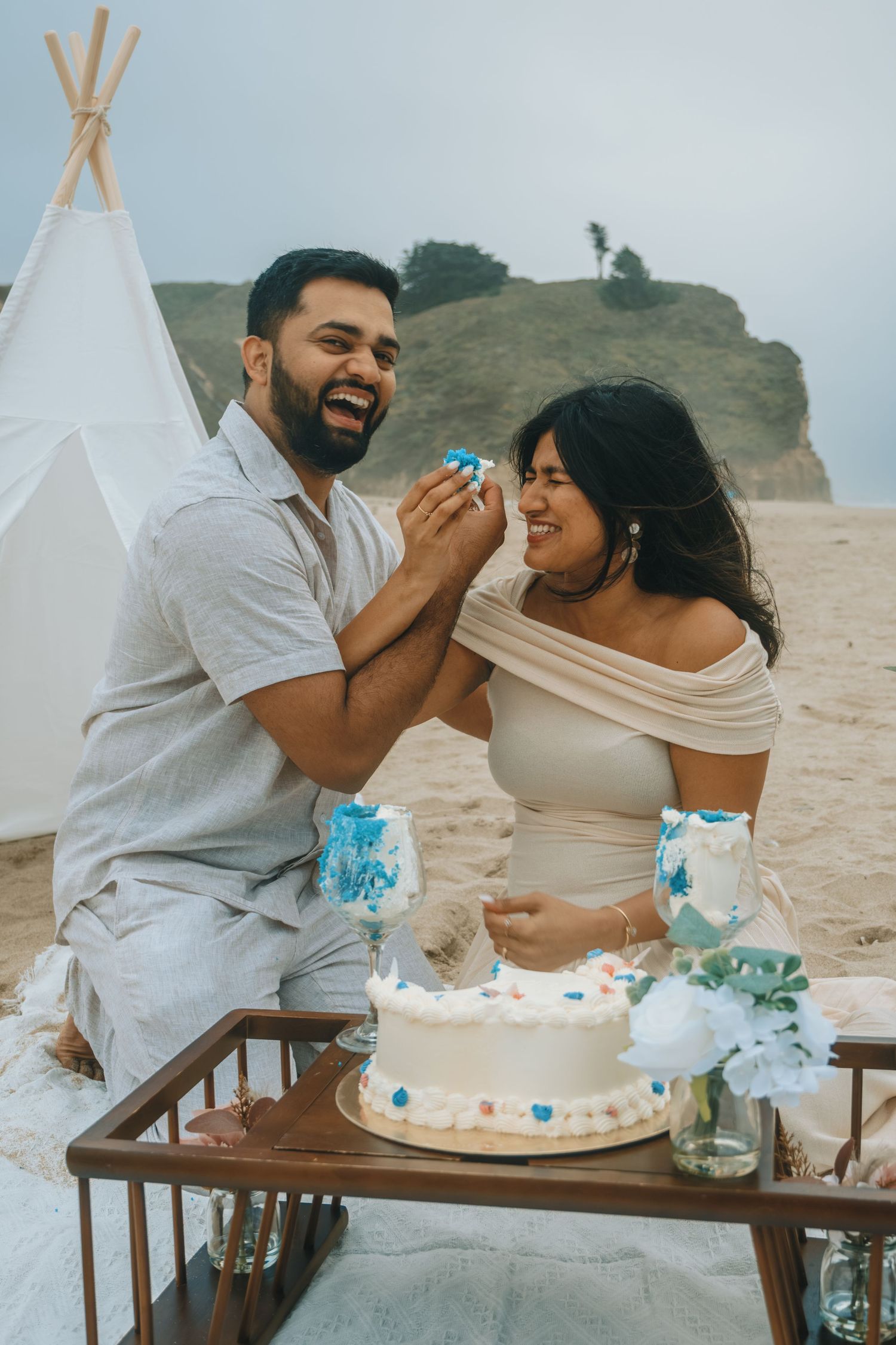 A couple shares a playful moment while smashing cake at an outdoor celebration.