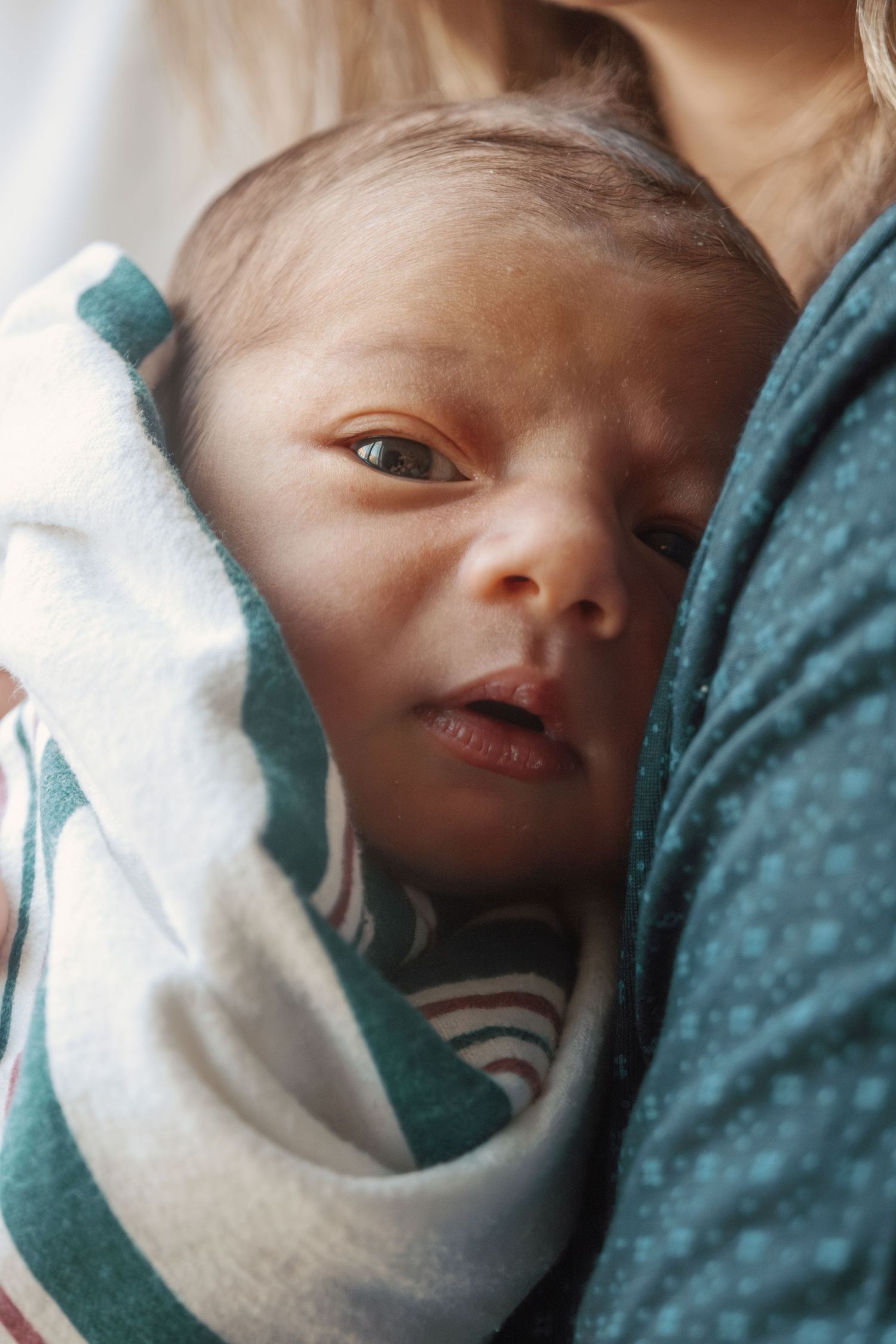 Newborn baby wrapped in white blanket against teal fabric background.