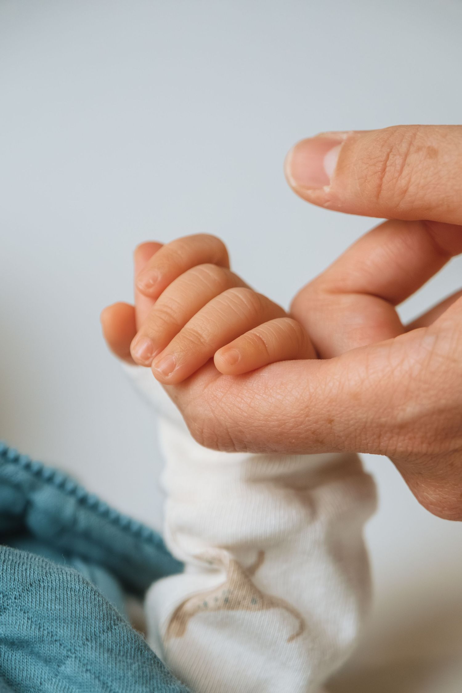 Gentle interaction between adult fingers and soft baby toes on light background.