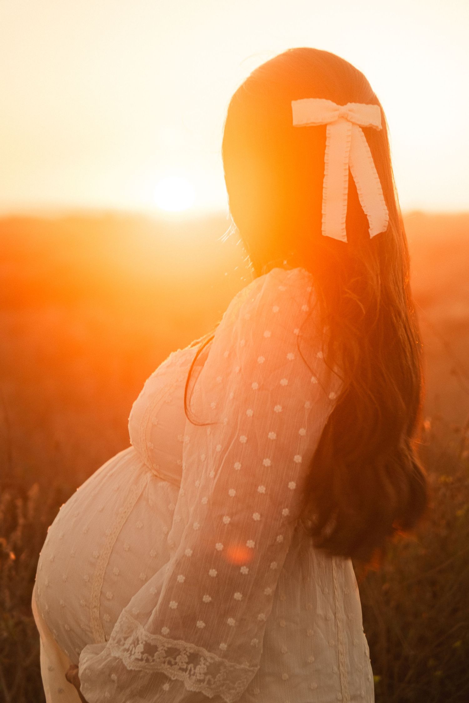 Silhouette of a person in white dress against an orange sunset sky.