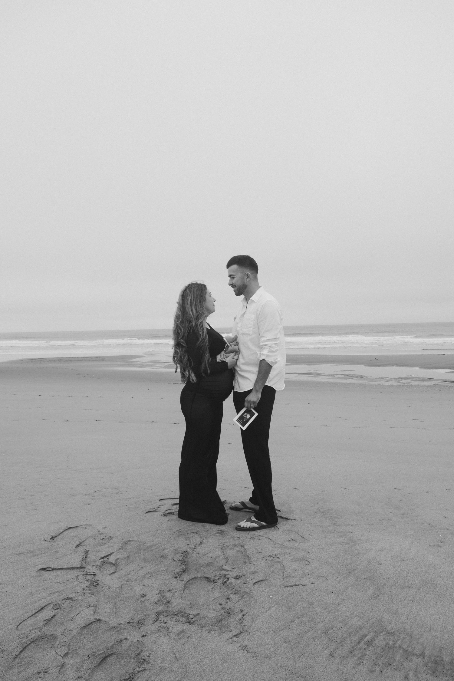 Couple sharing intimate moments on misty beach in black and white.