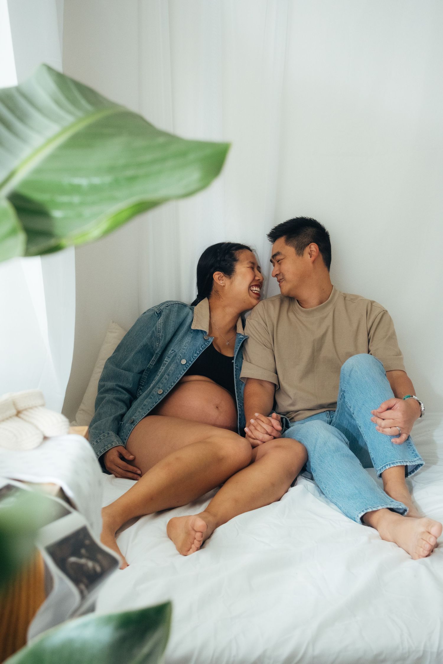 Couple relaxing together on white bedding with a green plant in the background.