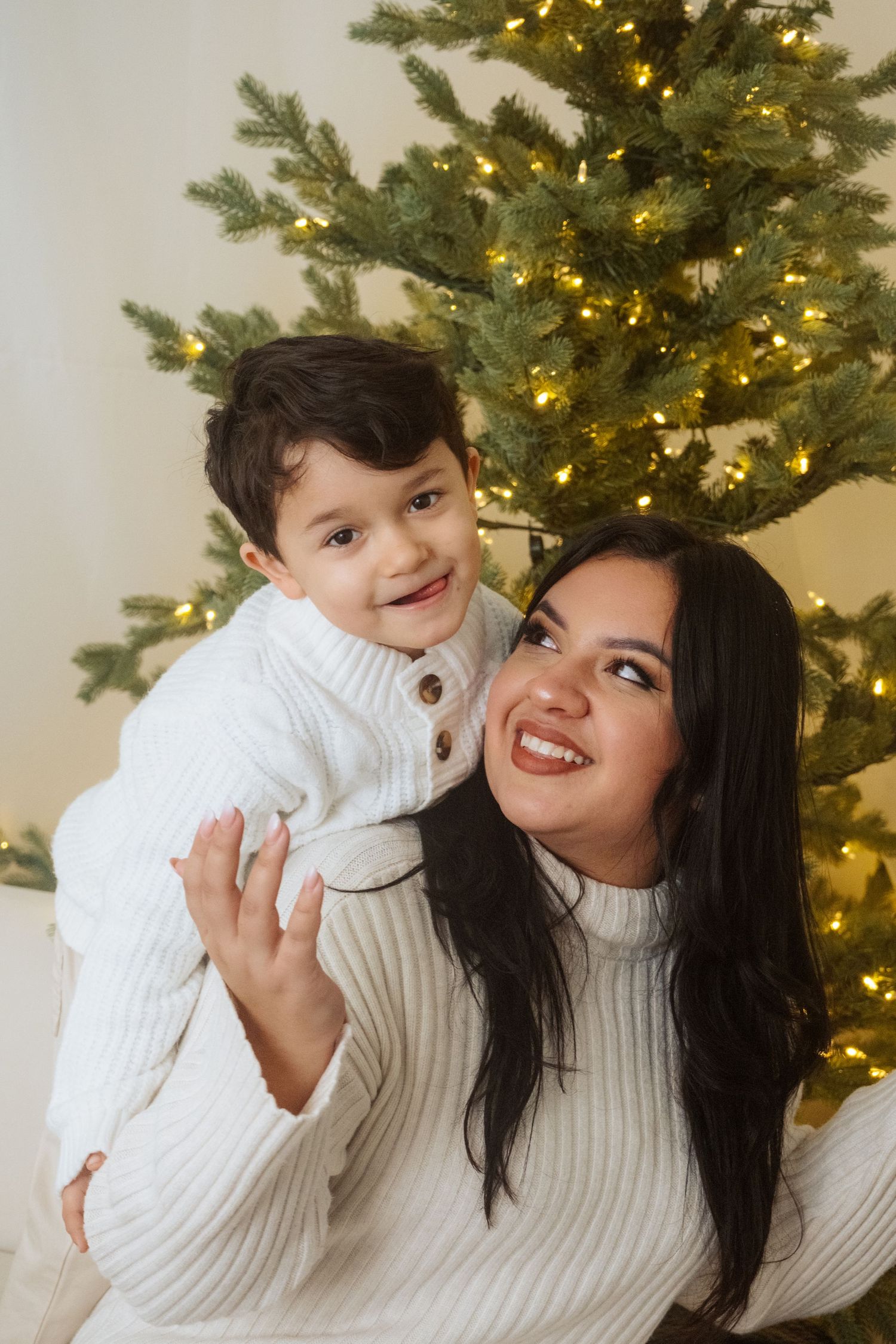 Heartwarming holiday portraits with white sweaters against lit Christmas tree.