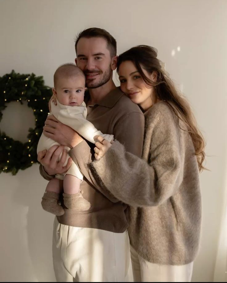 A cozy family portrait in front of a holiday wreath with warm sweaters and soft lighting creating an intimate atmosphere.