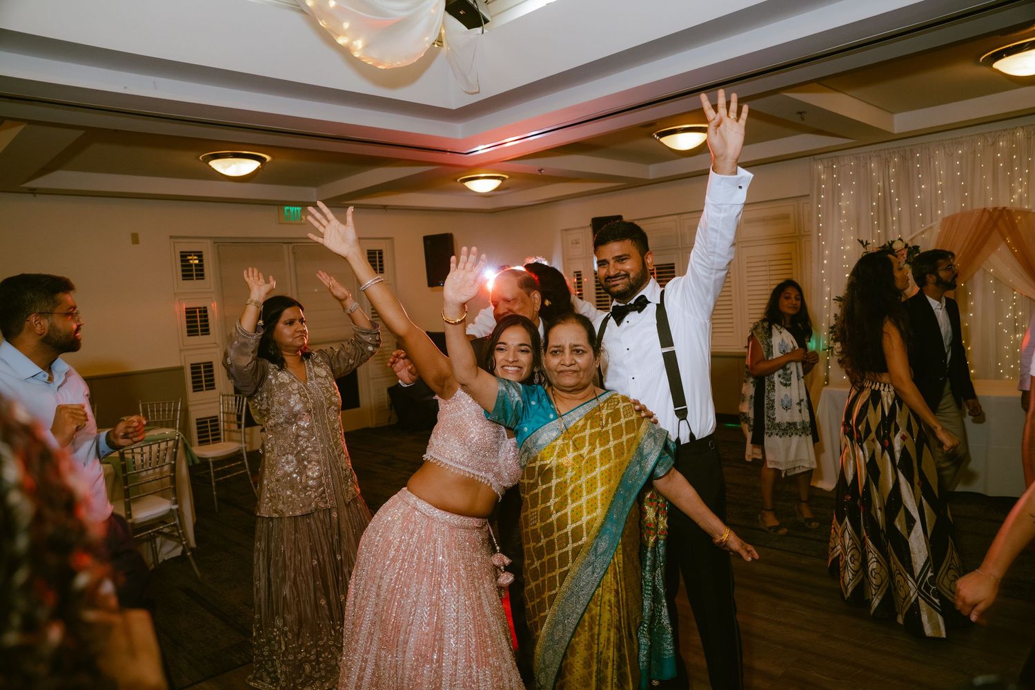 Guests dancing joyfully at an Indian wedding reception in a decorated banquet hall.