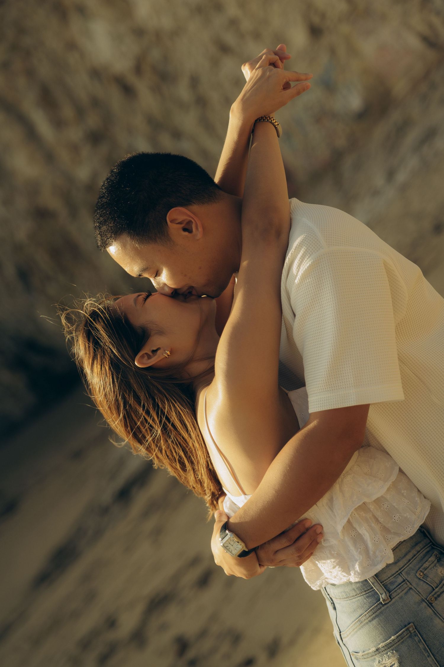 Romantic couple sharing a tender kiss outdoors, man in white shirt embracing woman in warm golden light.