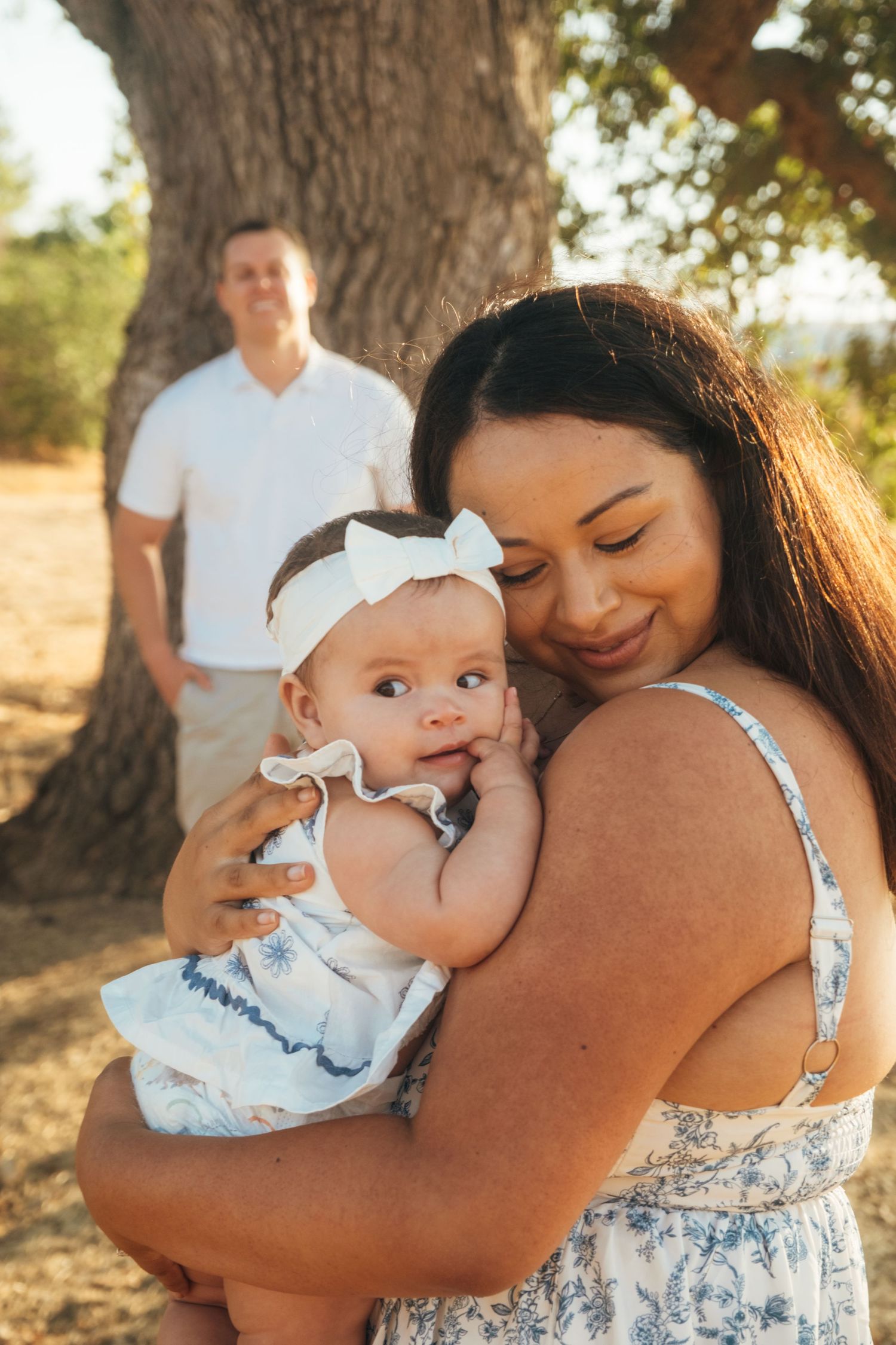 Mother and baby share tender moments under a large oak tree in warm sunlight.