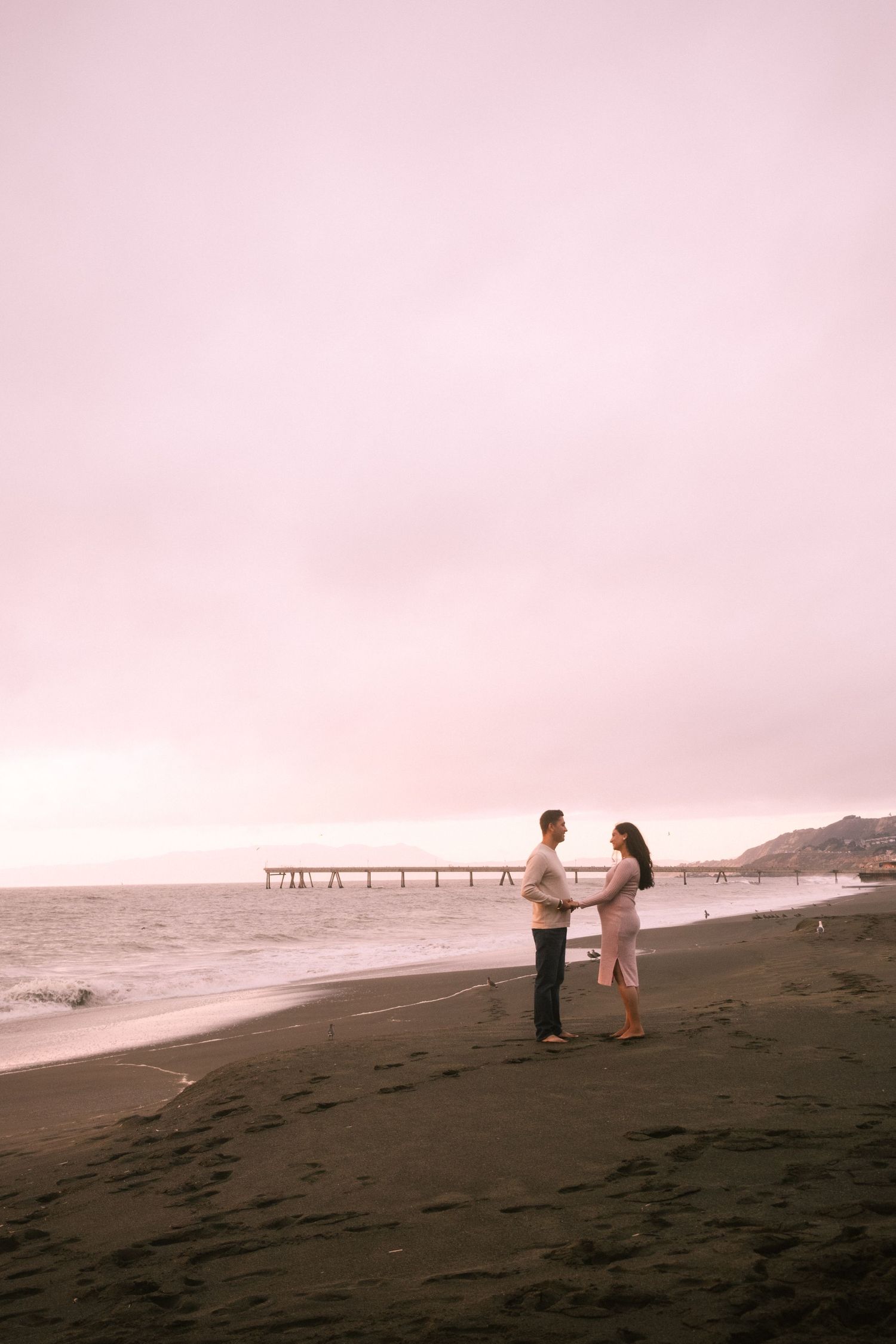 Silhouetted figures share tender moments on a dark sandy beach during sunset.